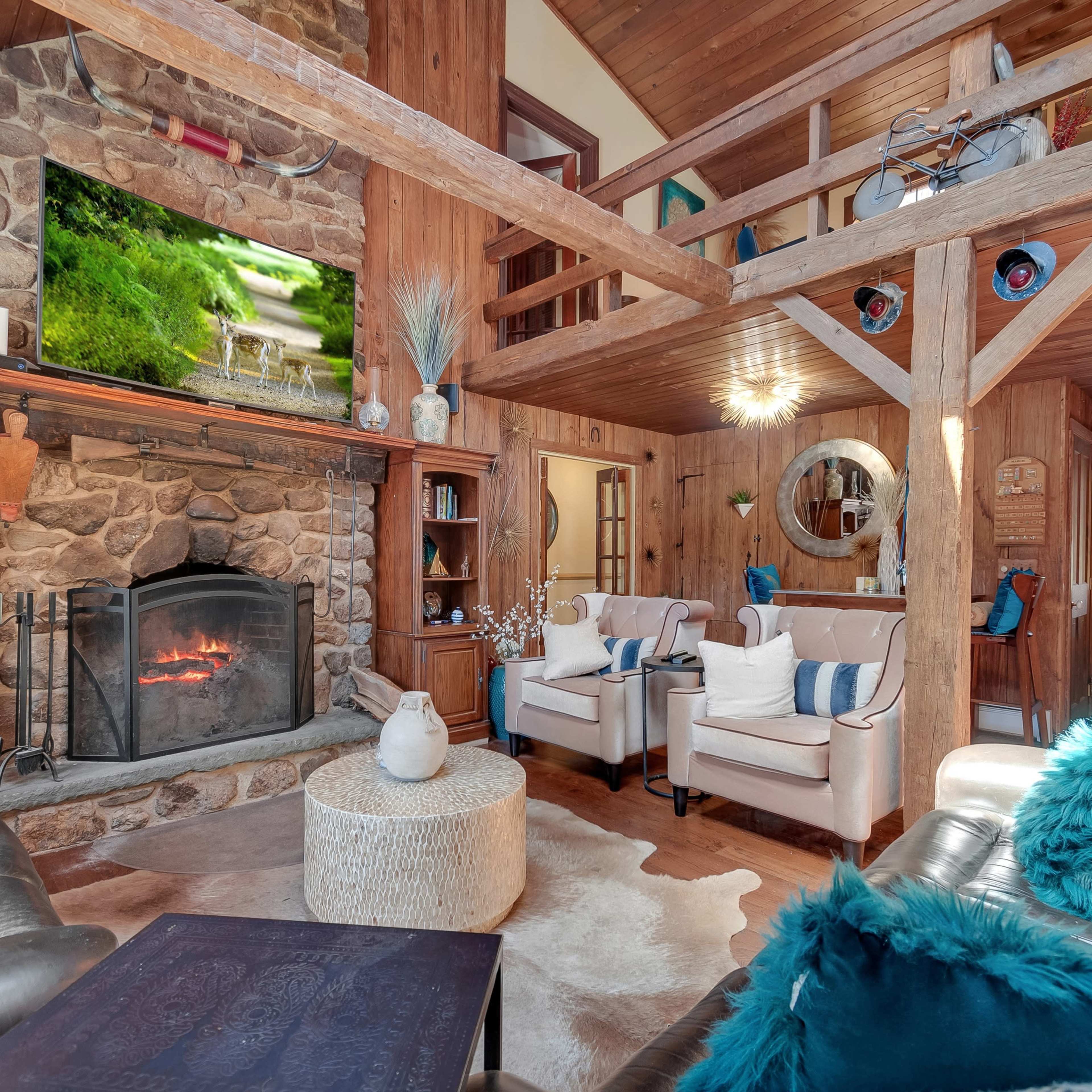 A rustic living room with a stone fireplace, wooden beams, and various seating arrangements around a central coffee table.