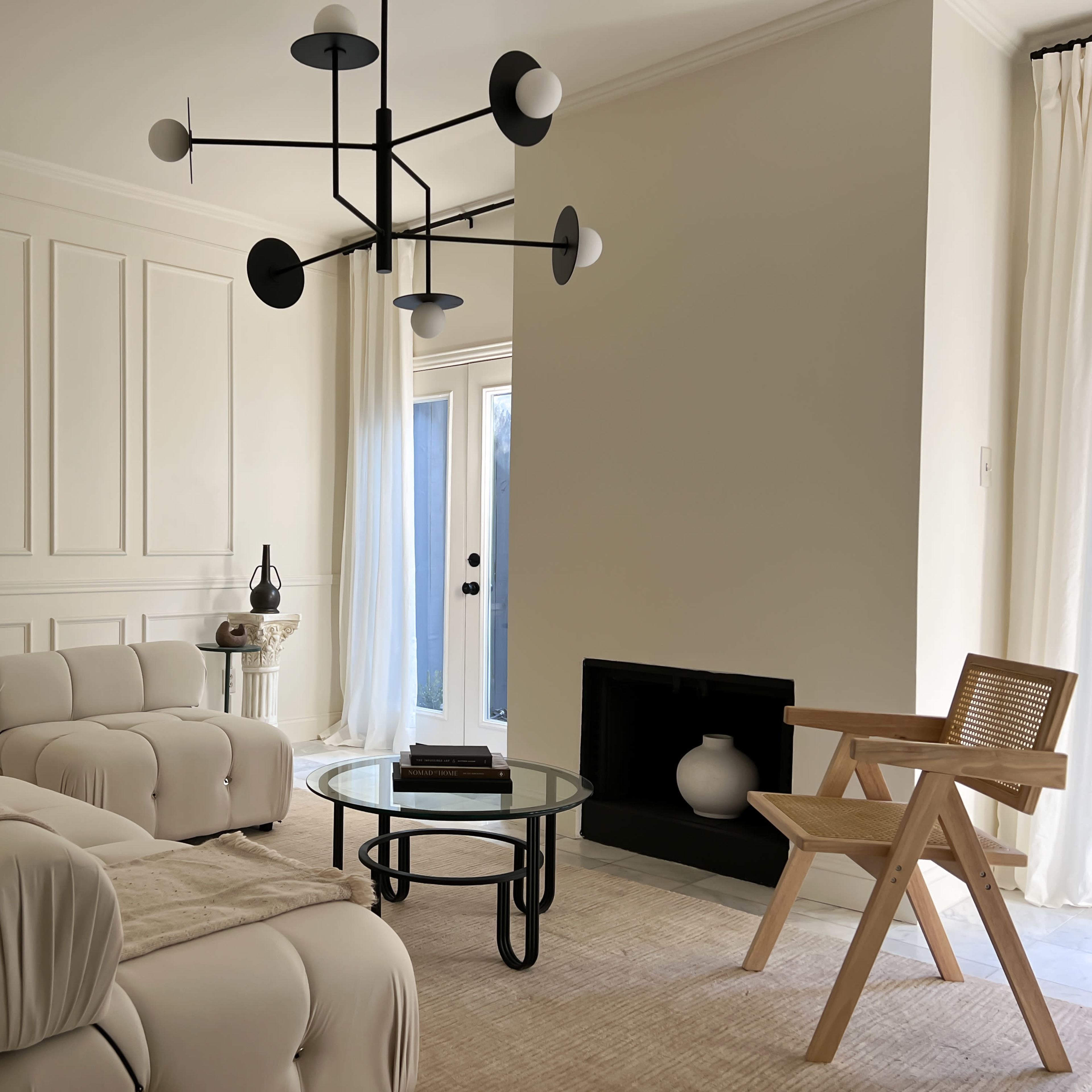 The living room features a modern design with a white sectional sofa, a round glass coffee table, a minimalist chandelier, and a wooden chair near a fireplace.
