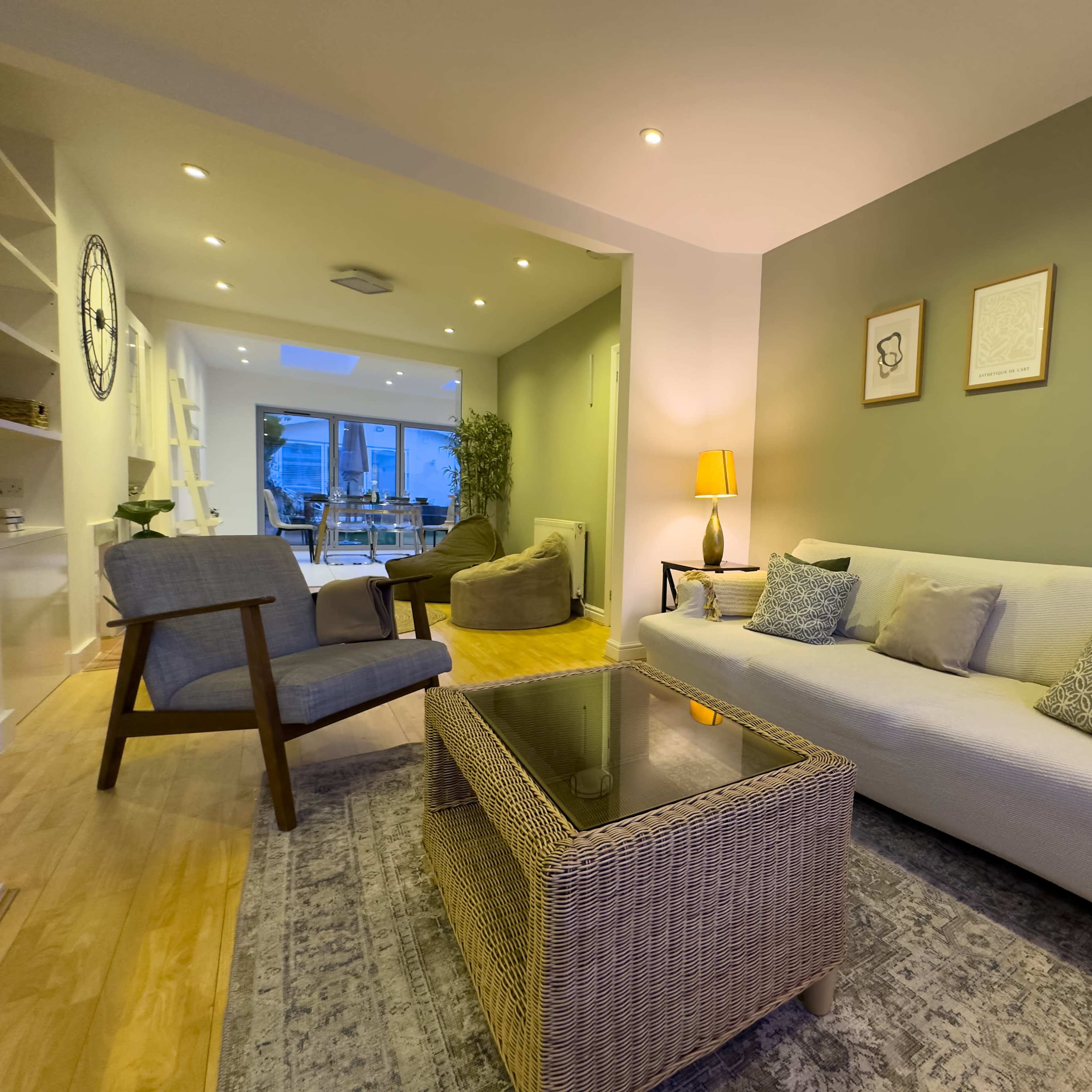 A modern living room with a white sofa, a glass-top coffee table, and a small reading chair, illuminated by soft lighting.