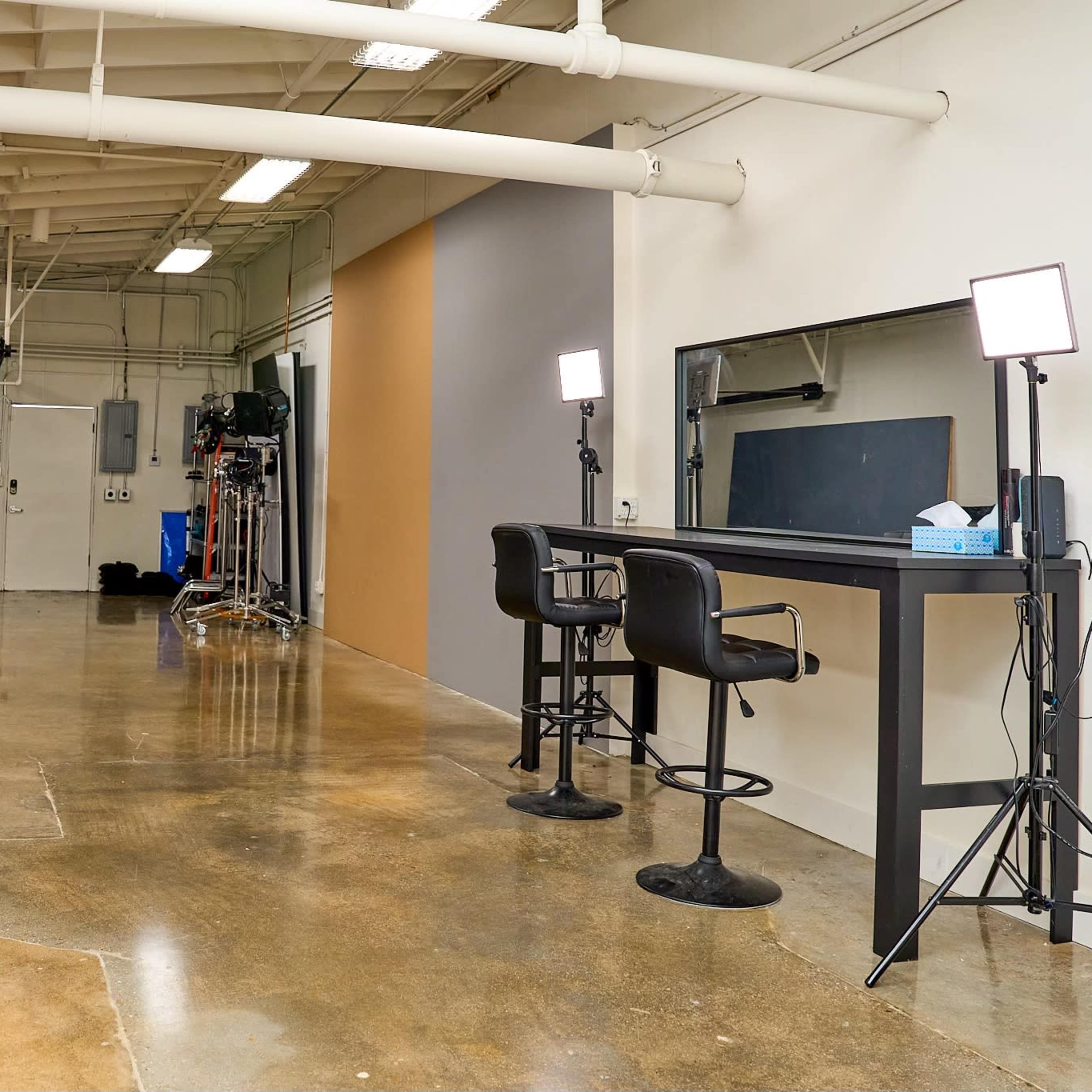A spacious, well-lit studio with a polished concrete floor, two black chairs, a large mirror, and a backdrop area.