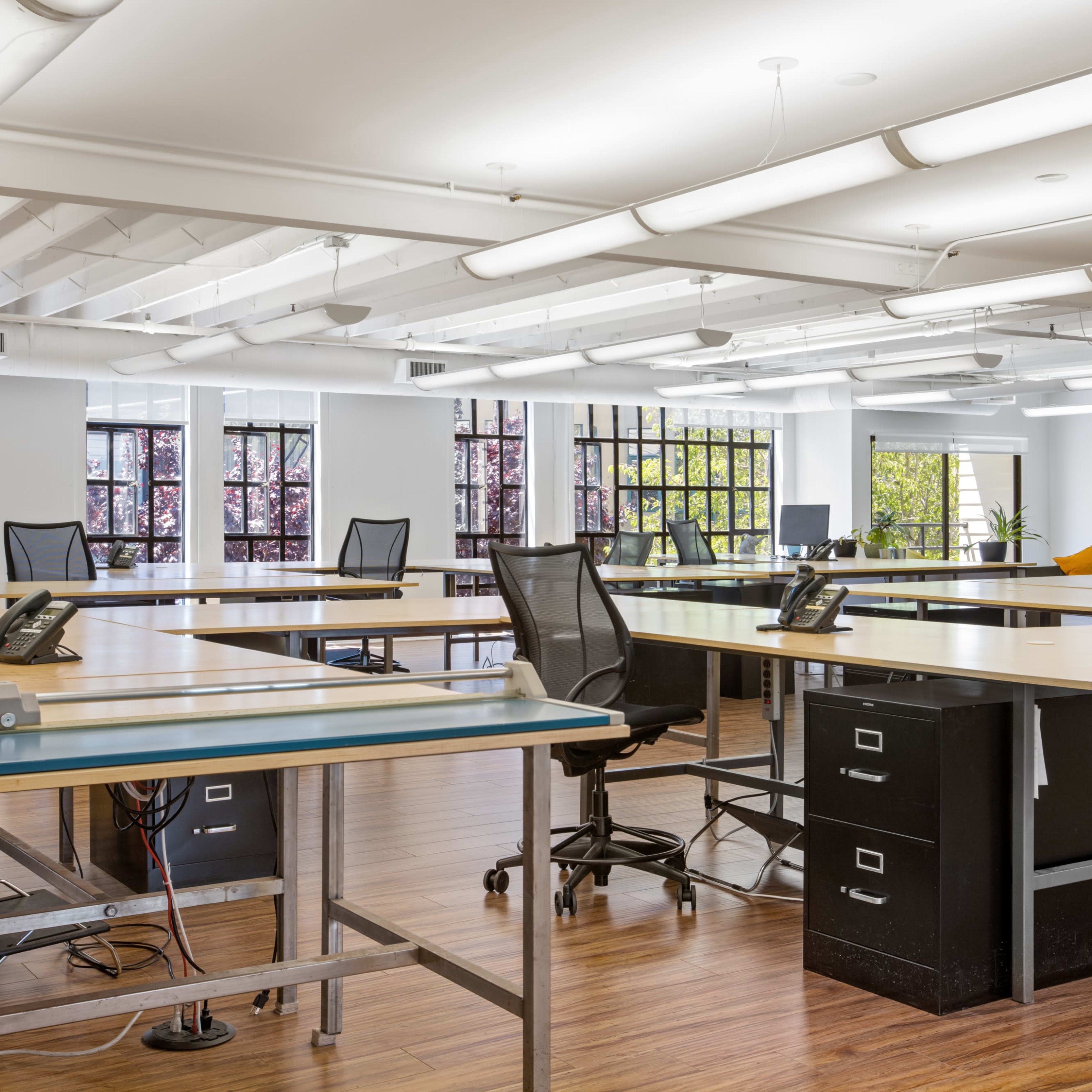 A spacious, modern office environment with multiple workstations featuring desks, chairs, and phones, and large windows allowing natural light.