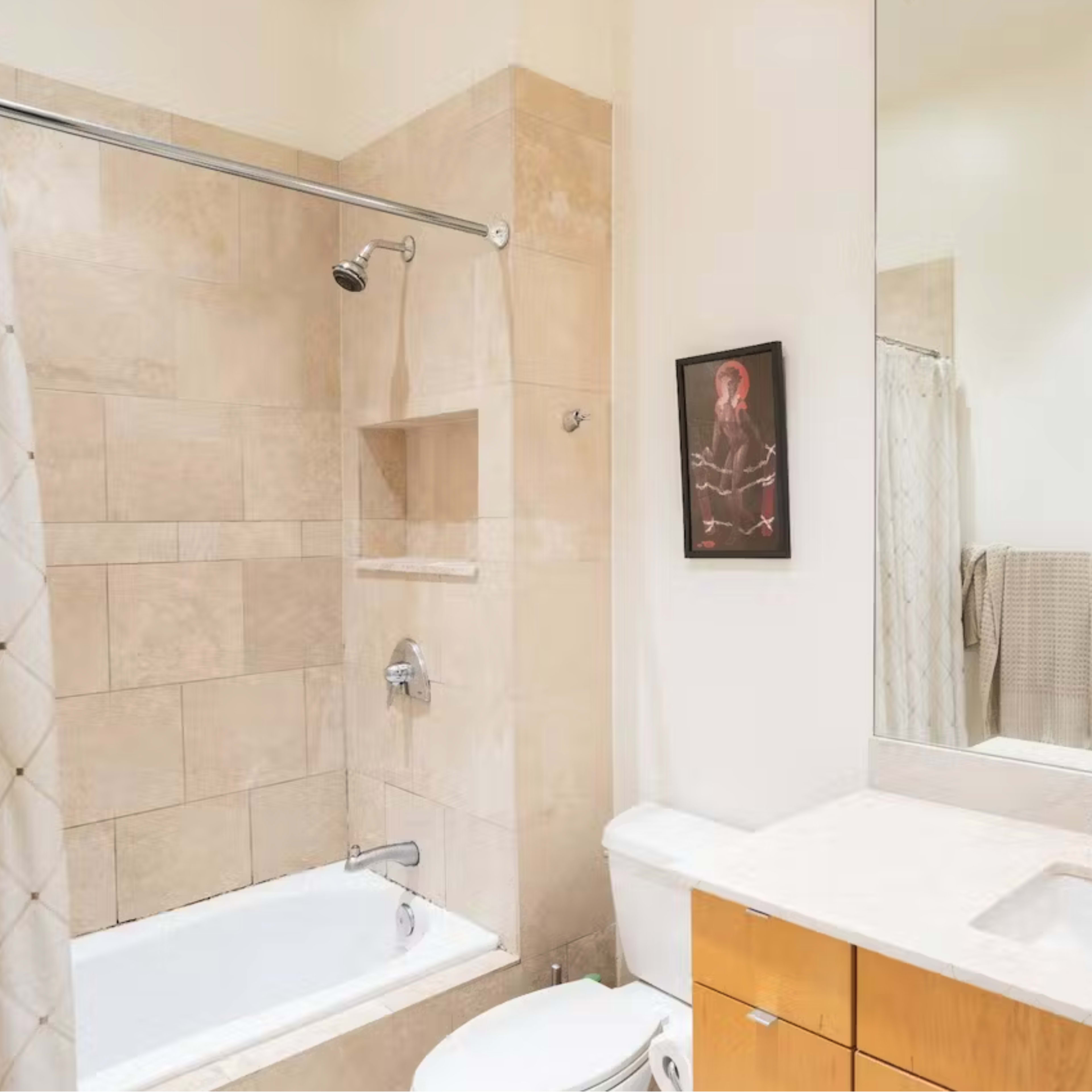The bathroom features a bathtub with a shower, beige tiled walls, a double sink vanity, and a large mirror.