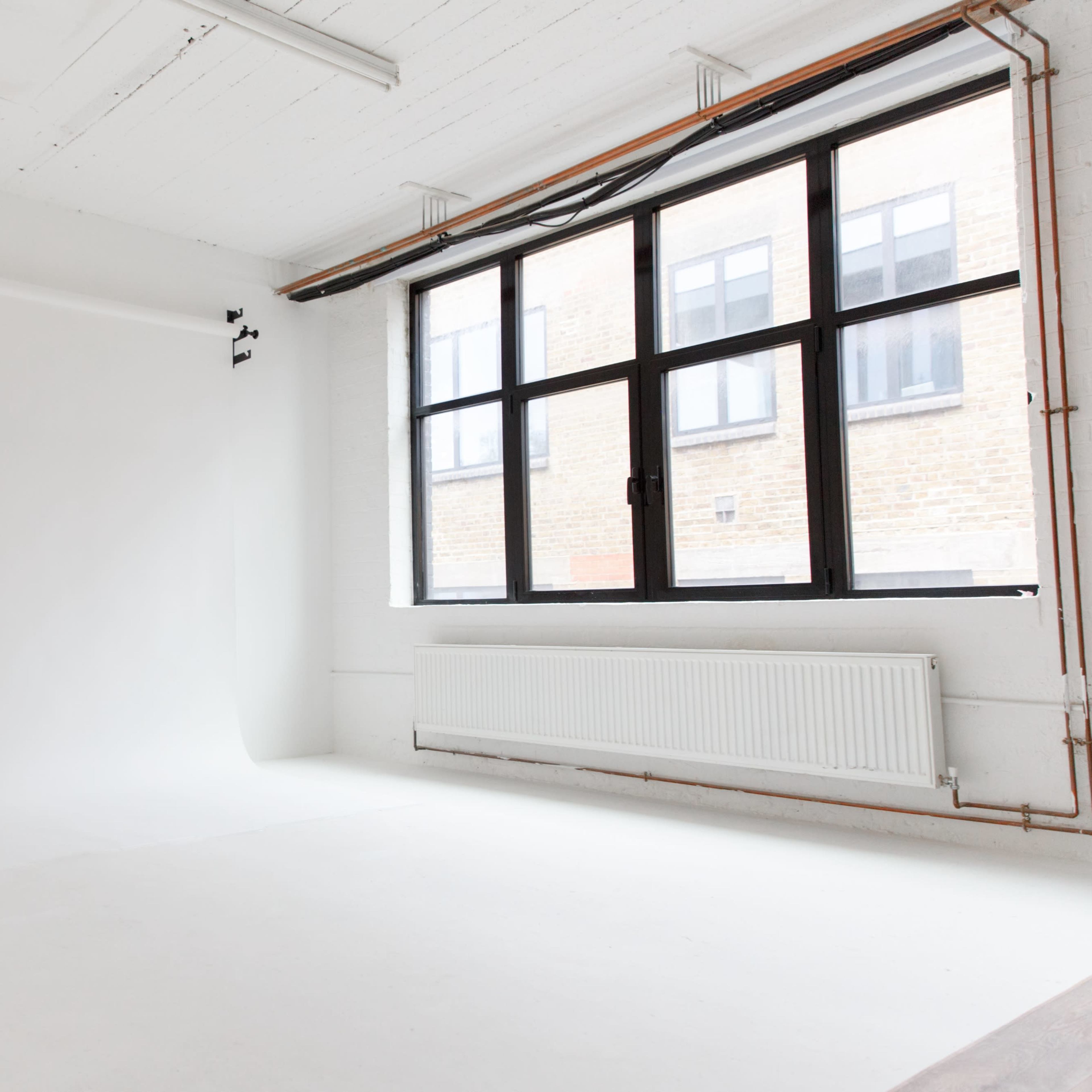 A bright, empty photography studio with a white backdrop and large windows letting in natural light.