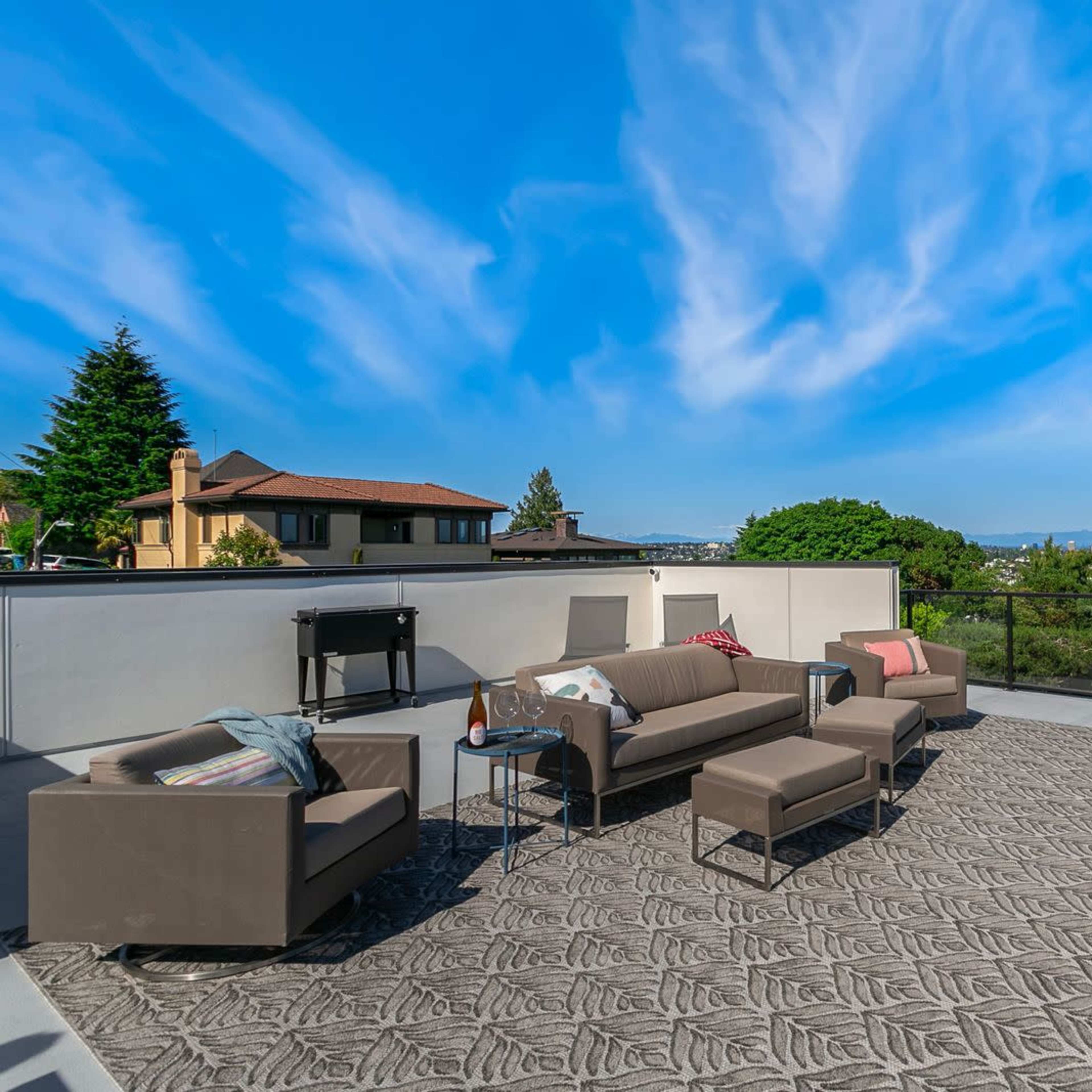 A spacious rooftop terrace features modern outdoor furniture and a scenic view of the surrounding landscape and homes.