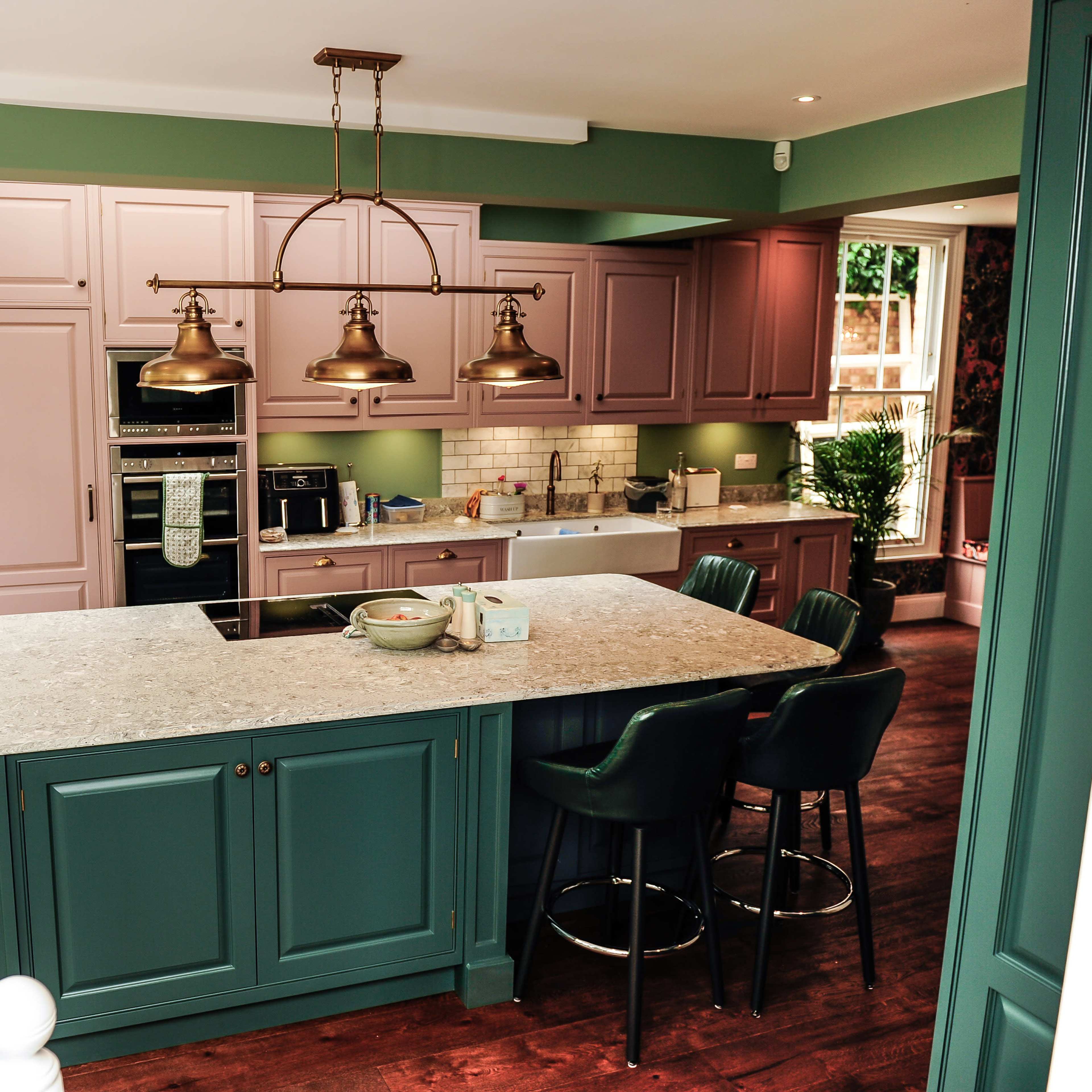 The kitchen features a spacious island with dark green cabinetry and pink upper cabinets, equipped with modern appliances and pendant lighting.