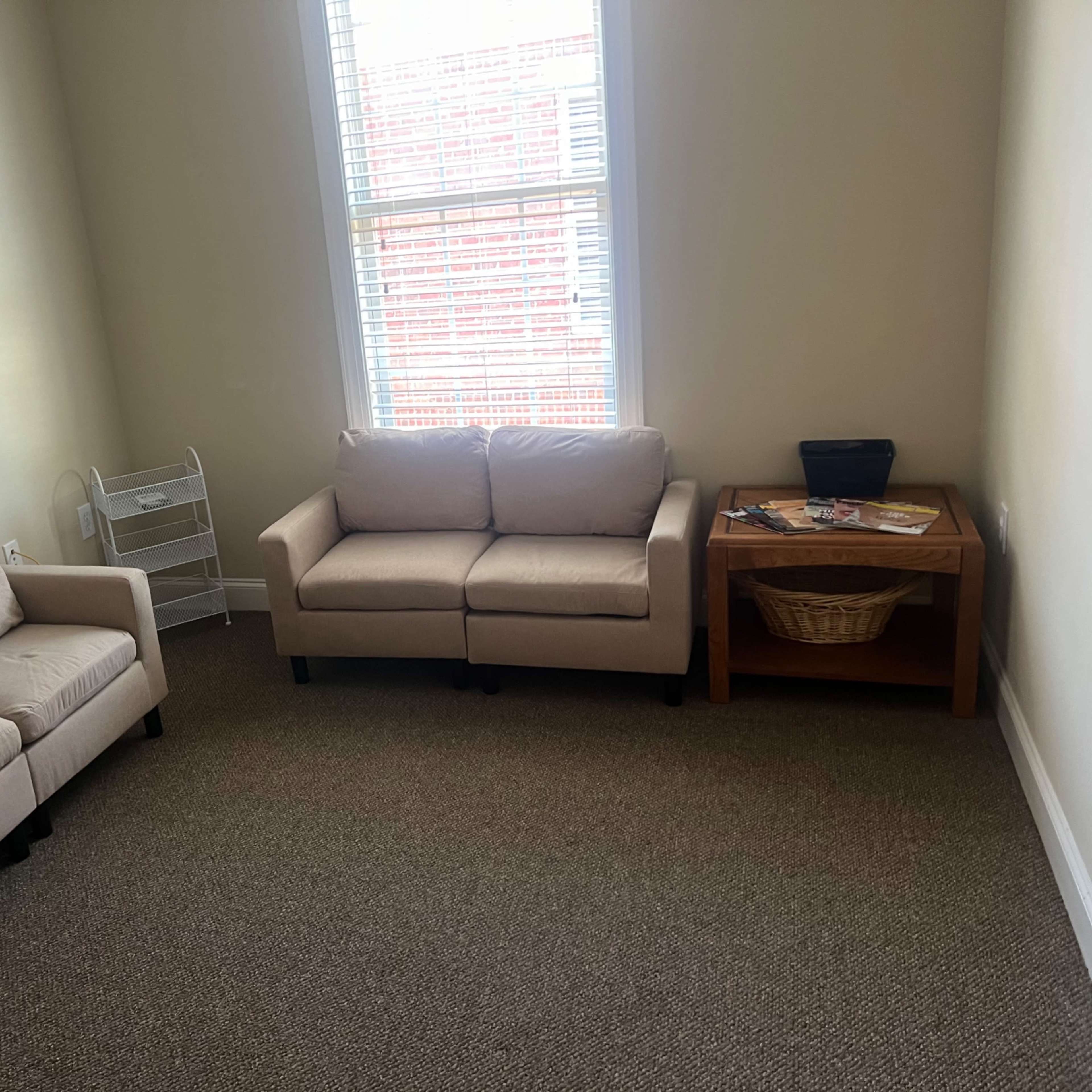 A small room with two beige sofas, a wooden table with a basket, and a window letting in natural light.