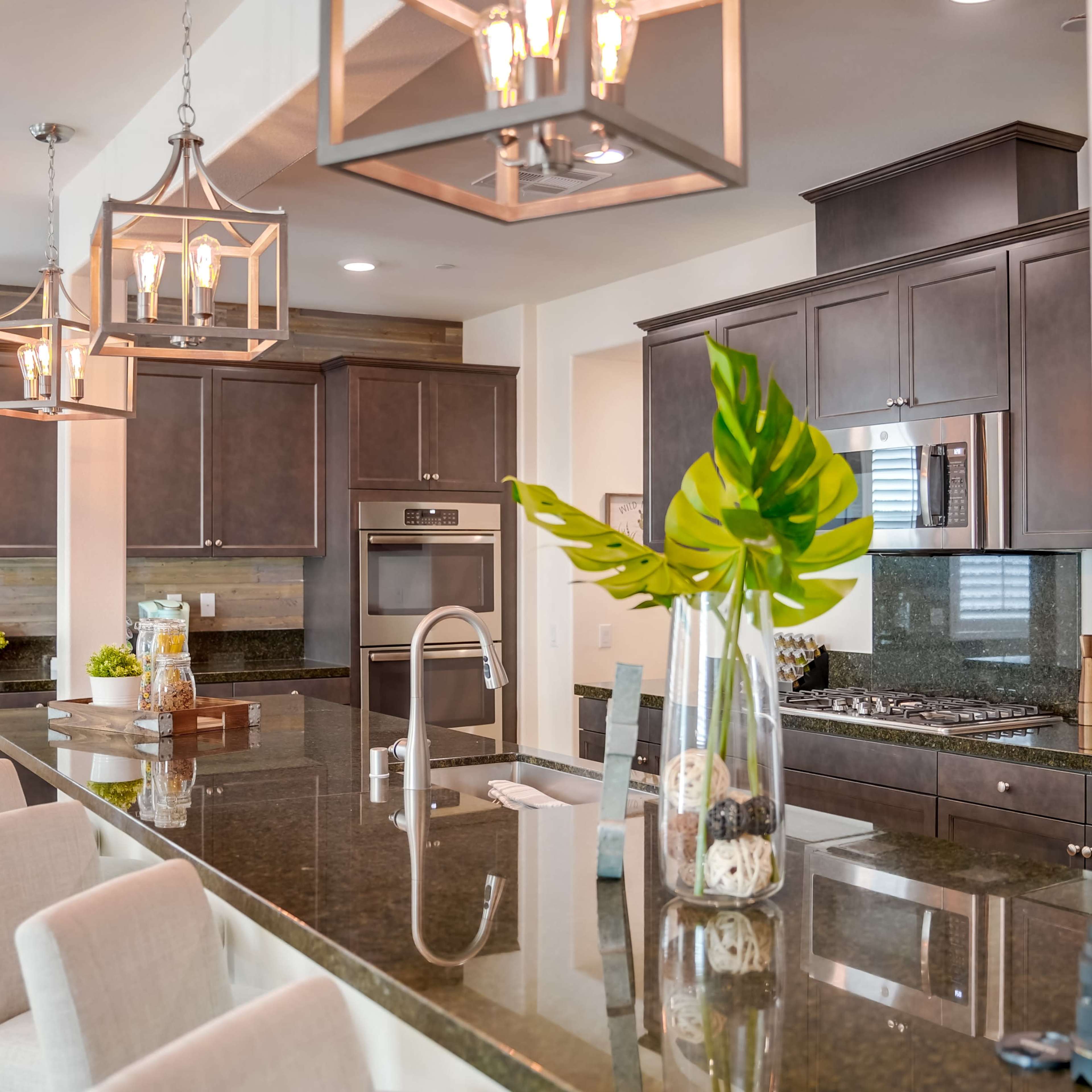 A modern kitchen with dark wooden cabinetry, a large granite island, and pendant lights above.