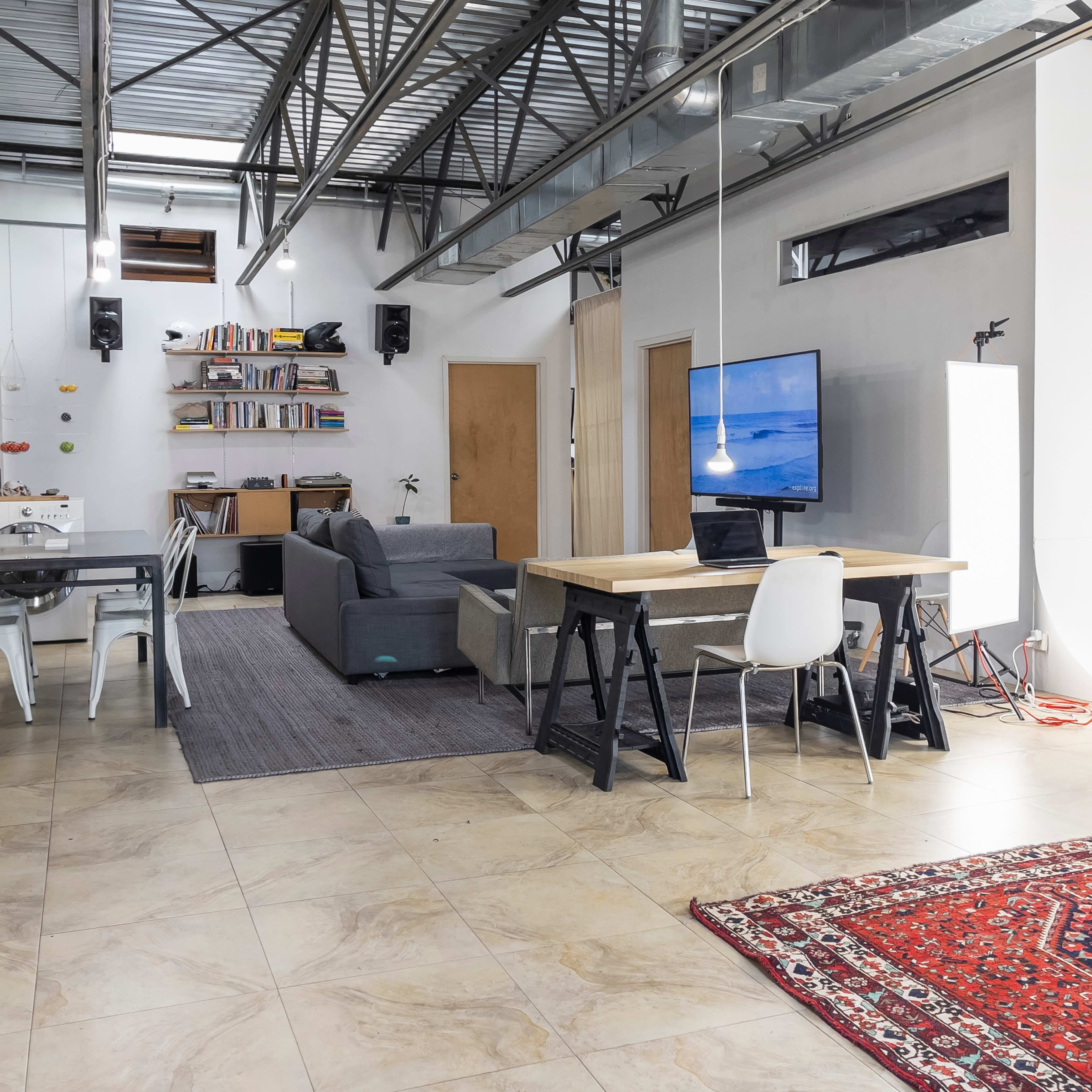 An open-concept living space featuring a dining area with a table and chairs, a sofa, a television, and bookshelves along one wall.