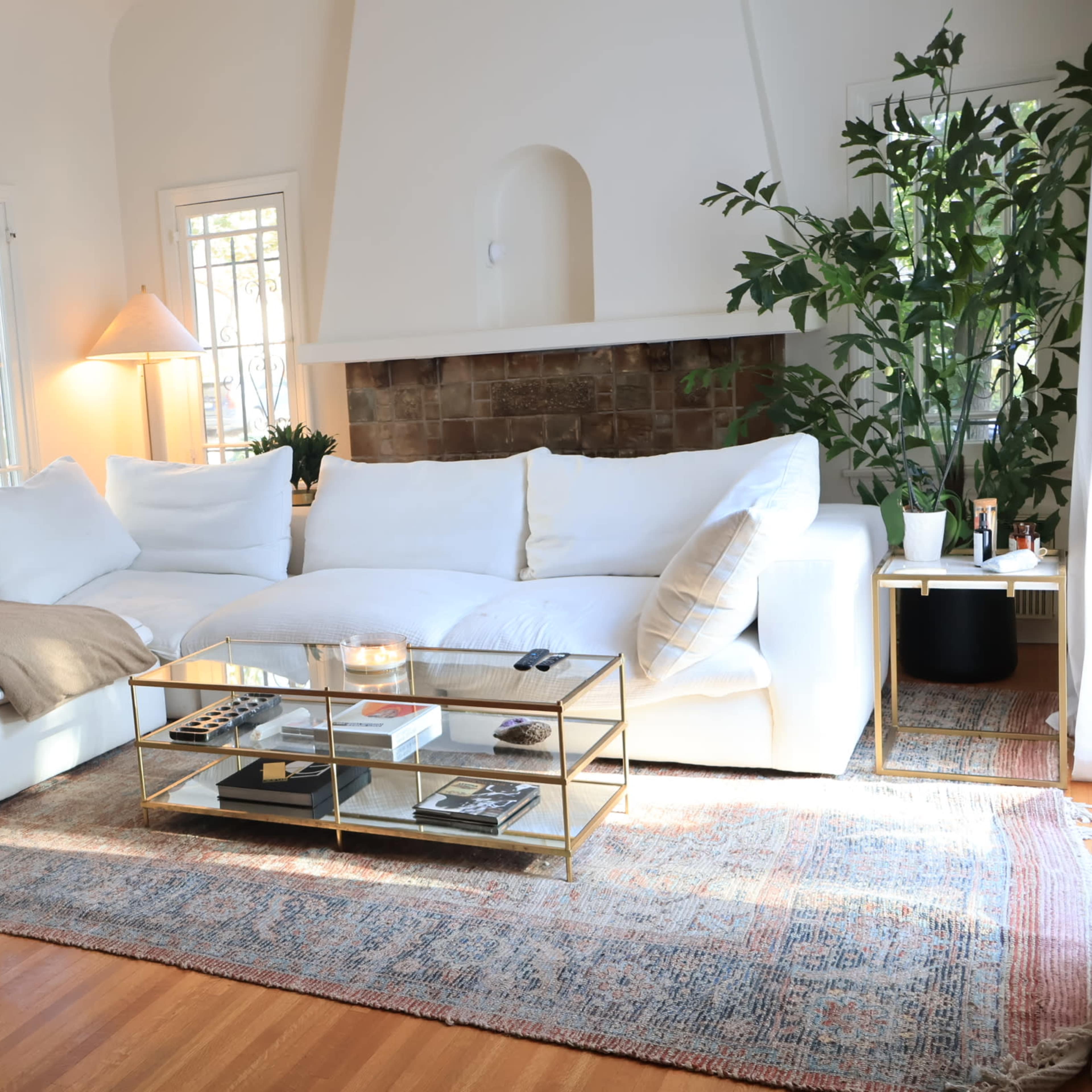 A bright living room with a large white sectional sofa, a glass coffee table, and greenery in the corner.