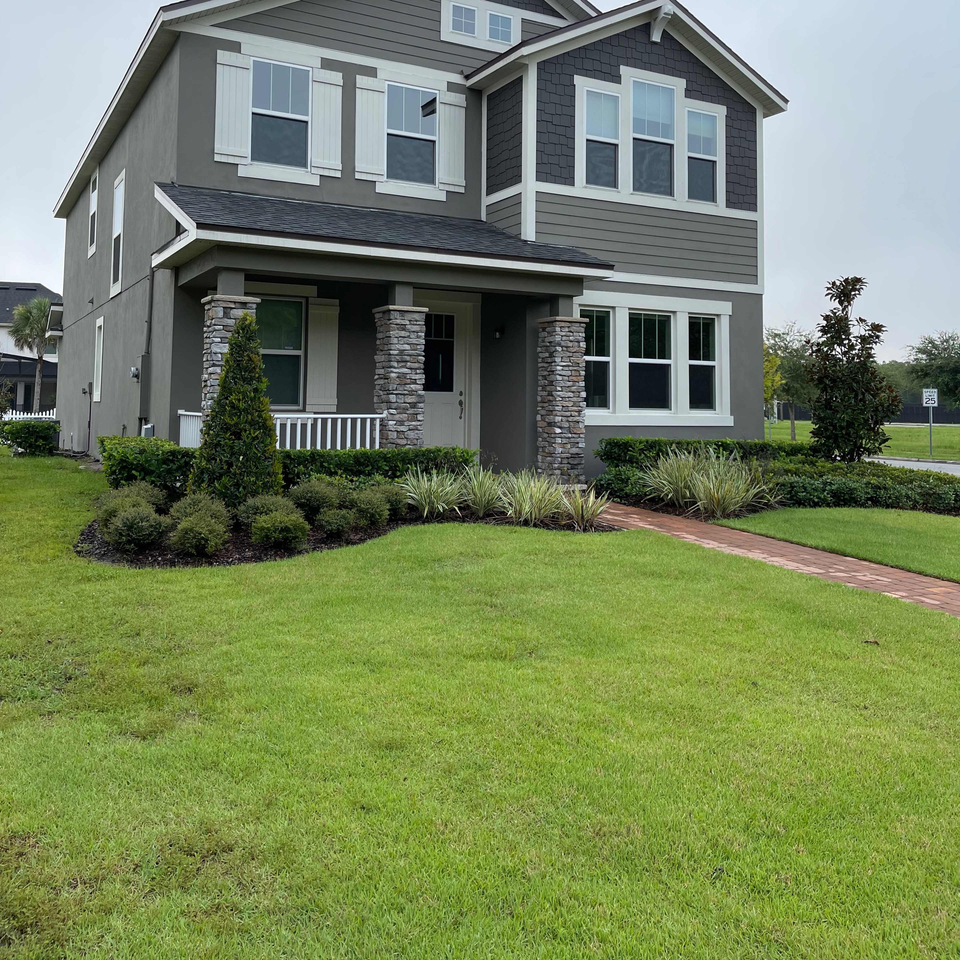 A two-story gray house with stone accents and a neatly landscaped front yard is depicted.