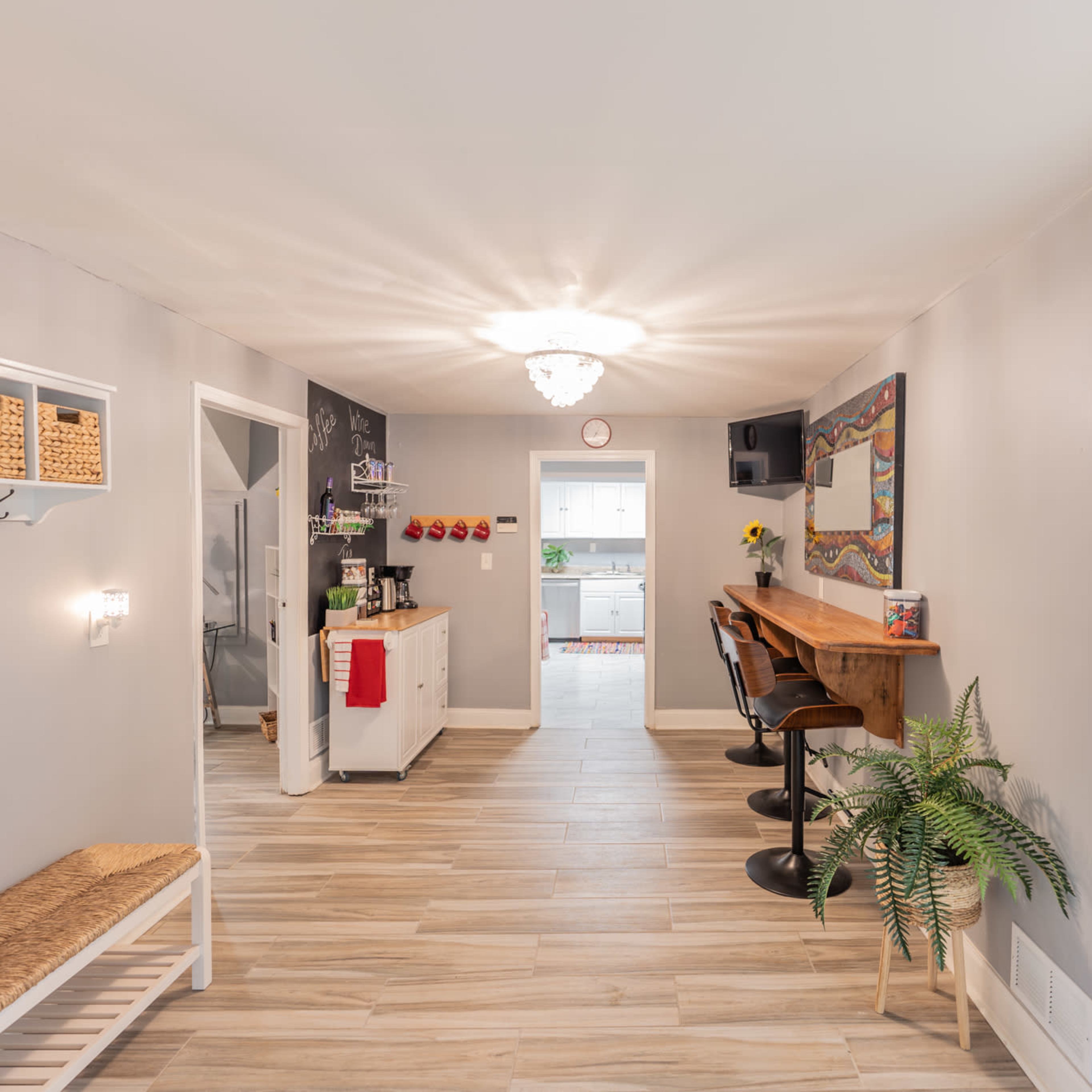 A well-lit interior hallway with a bench, wall-mounted storage, and a doorway leading to a kitchen area.