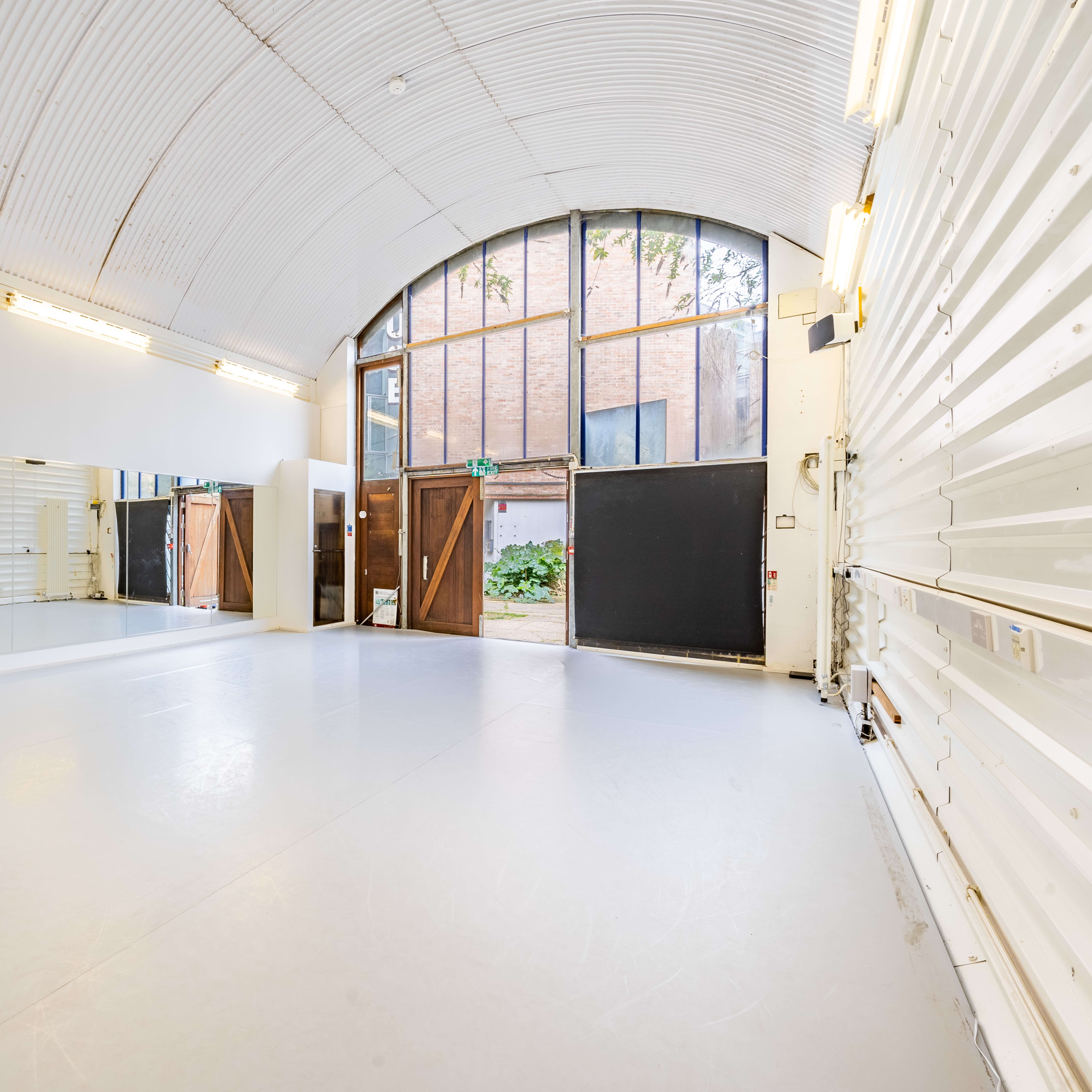 A spacious dance studio with a large mirror on one wall and double doors leading to an outdoor area.