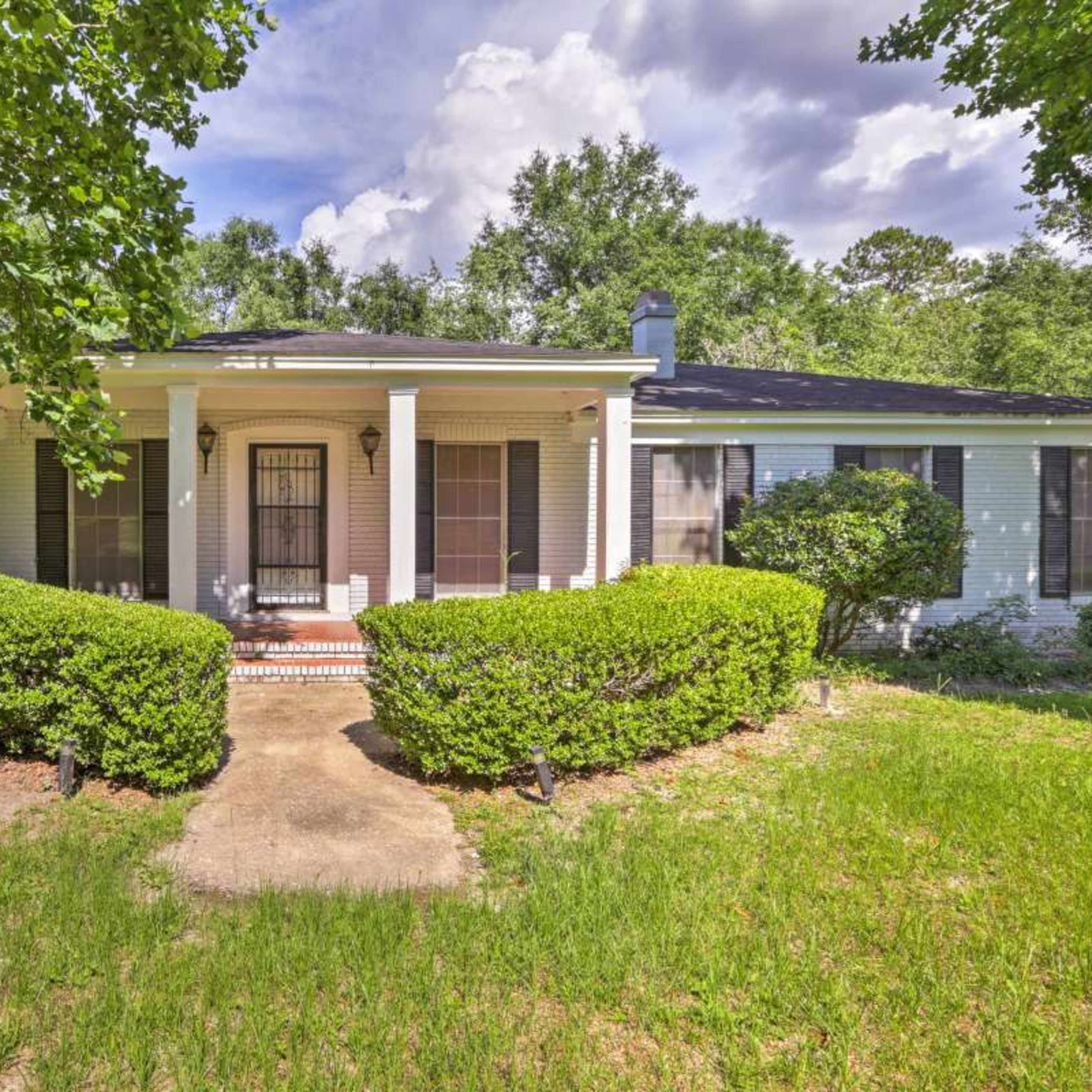 A single-story house with a front porch is surrounded by well-maintained shrubs and grass under a partly cloudy sky.
