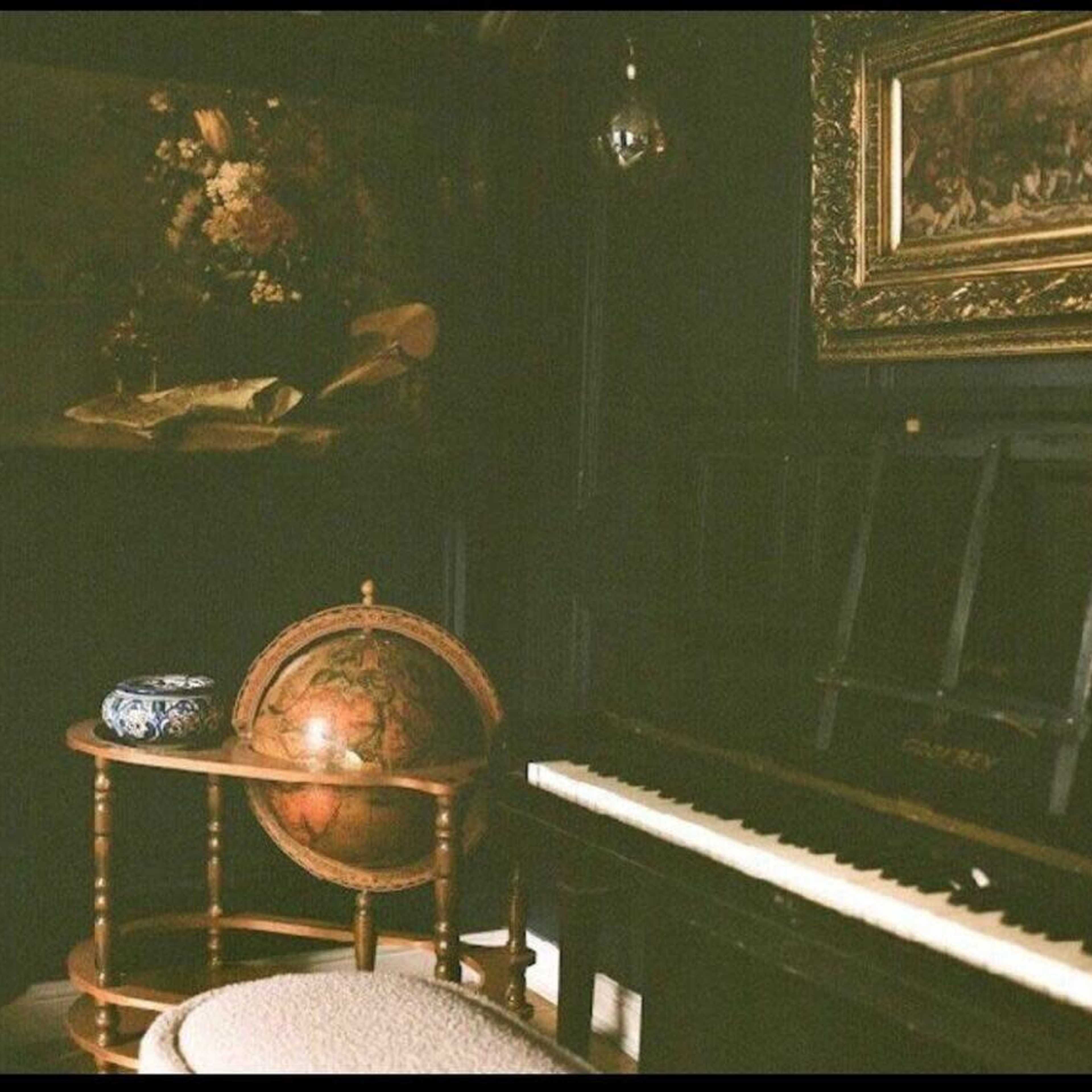 A dimly lit room with a globe on a wooden stand next to a piano and an ornate painting on the wall.