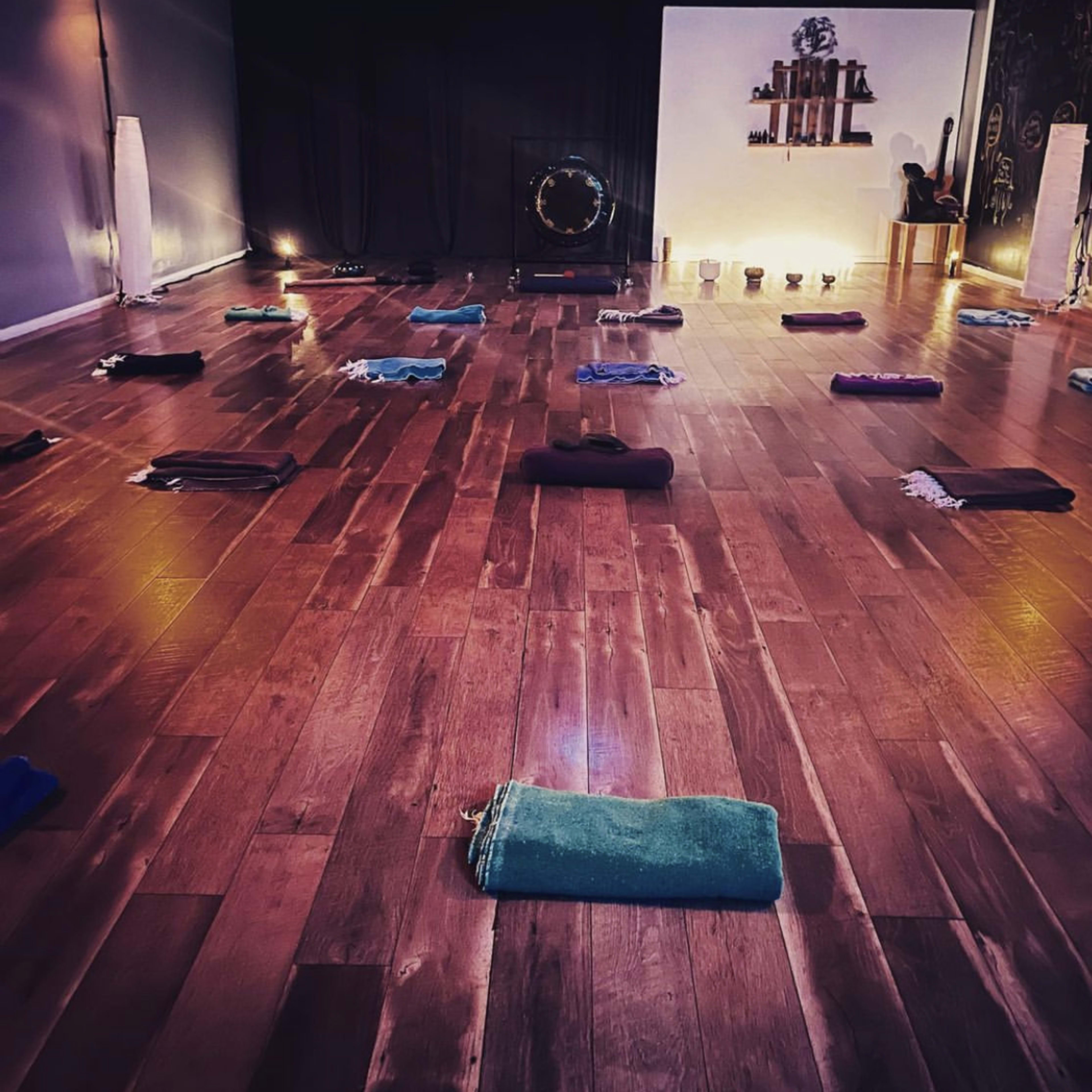 A yoga studio with neatly arranged mats on a wooden floor, candles, and a wall adorned with minimalist decor.