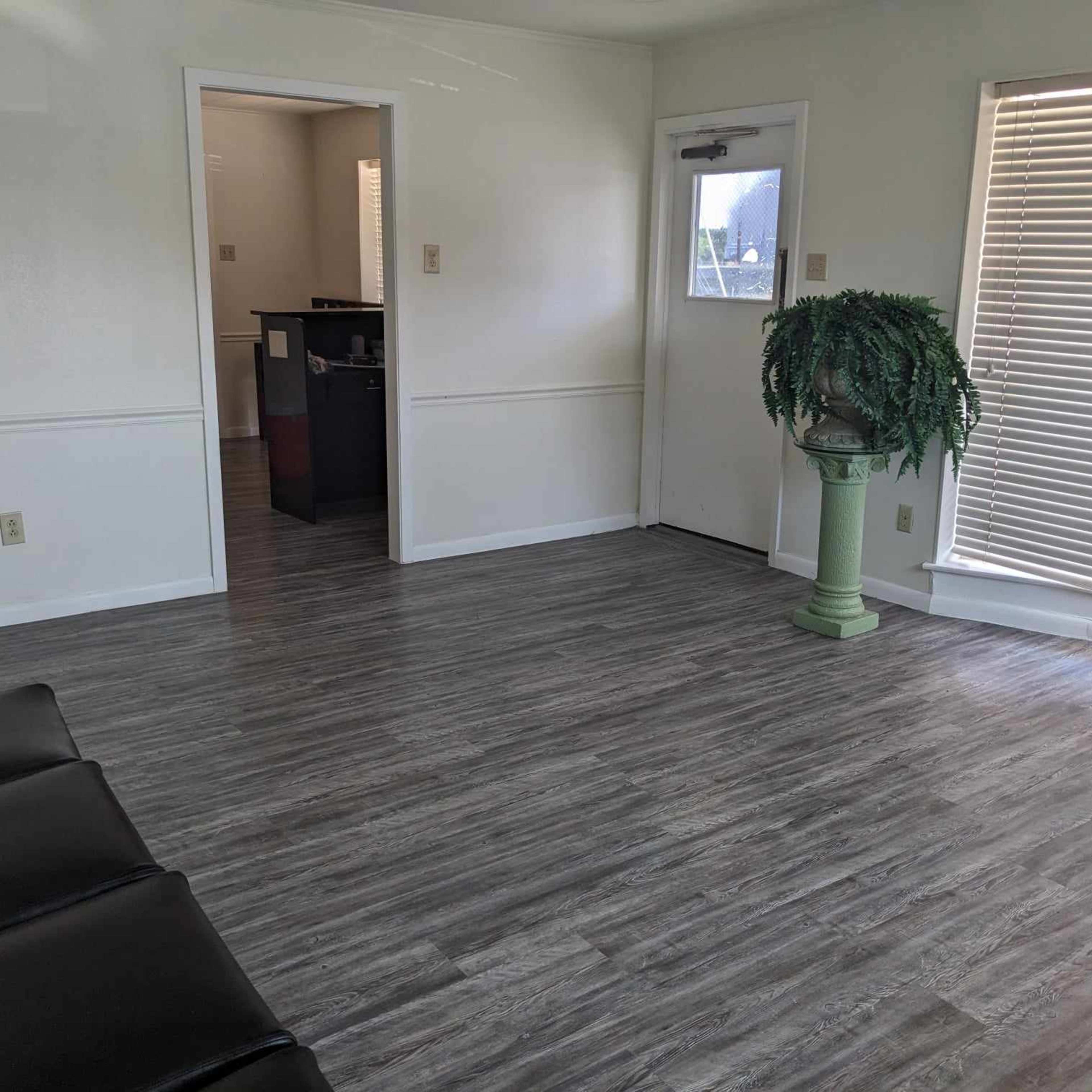 A spacious room with a wooden floor, a potted plant in the corner, and a doorway leading to another area.
