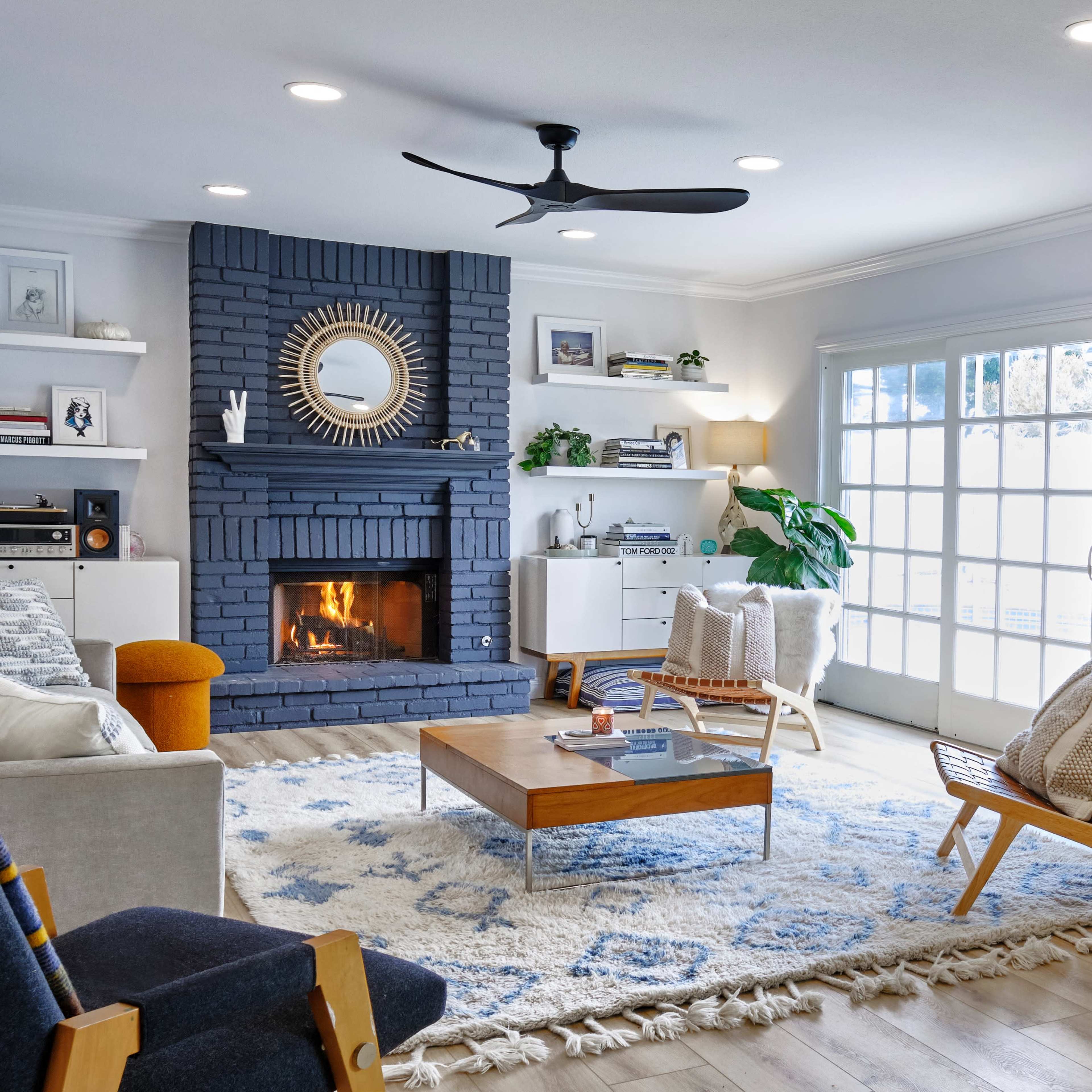 A modern living room features a brick fireplace, a large wall-mounted TV, comfortable seating, and a wooden coffee table on a patterned rug.
