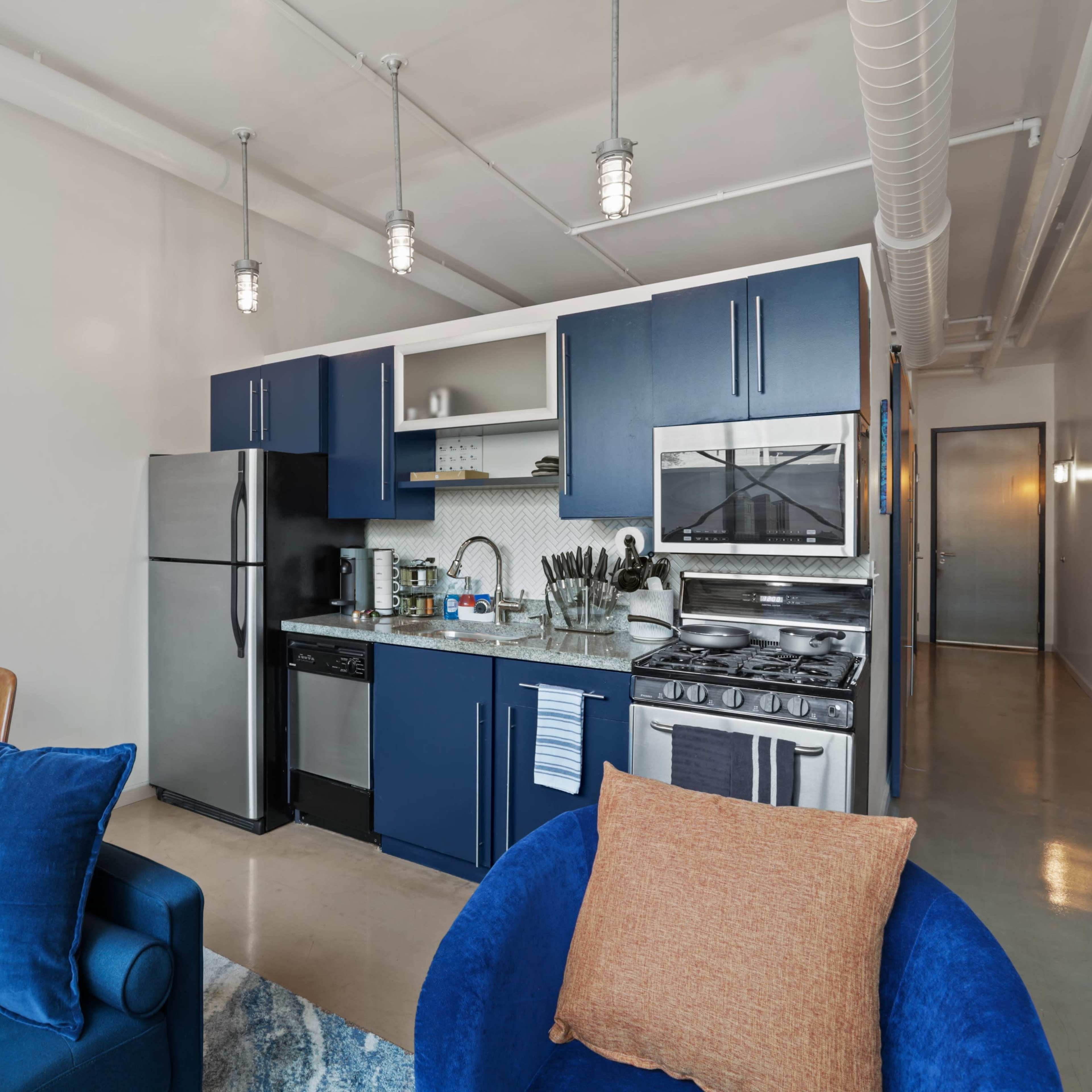 A compact kitchen and dining area featuring blue cabinetry, stainless steel appliances, and a small table set for two.