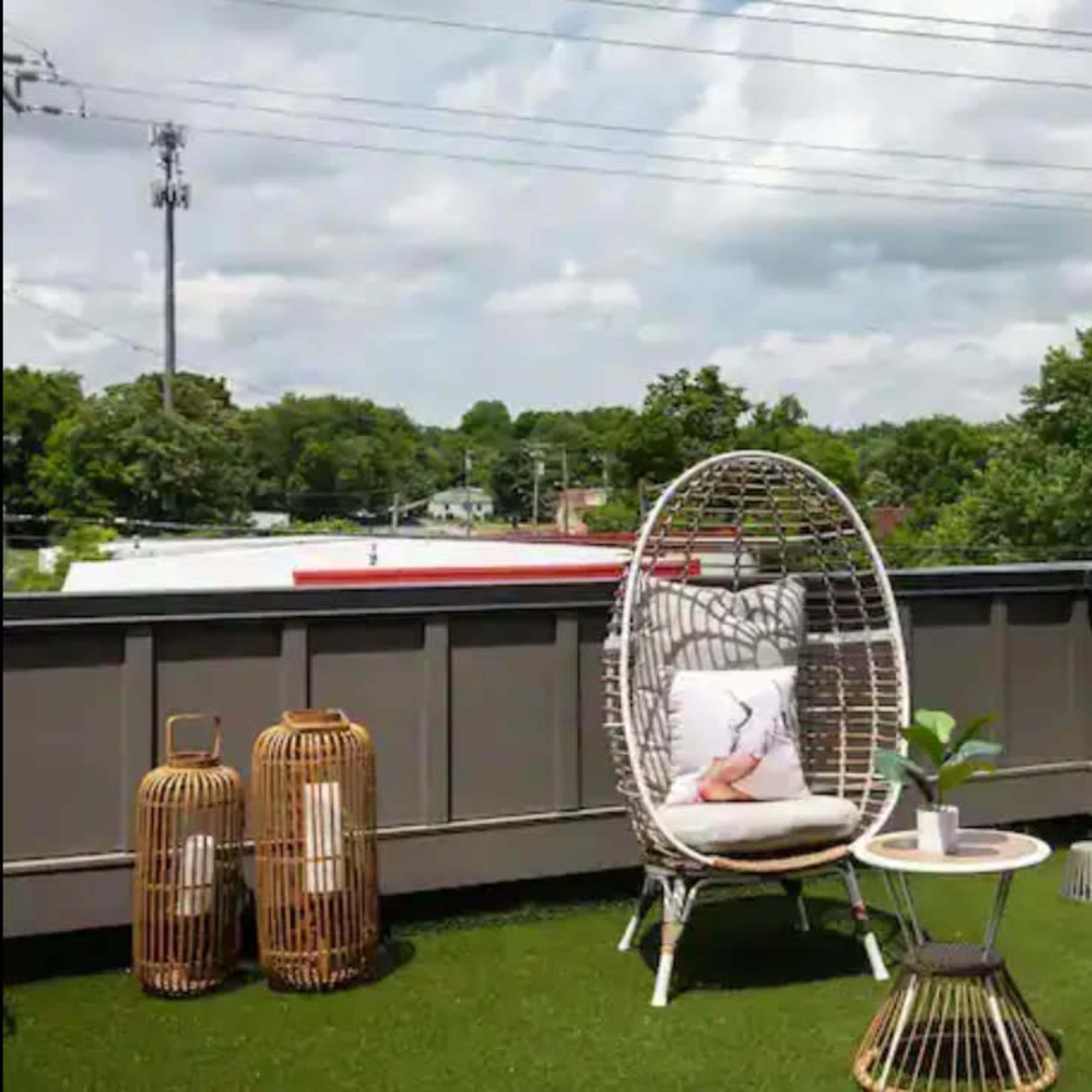 Two woven chairs on a balcony surrounded by greenery, with a small table and decorative items nearby.