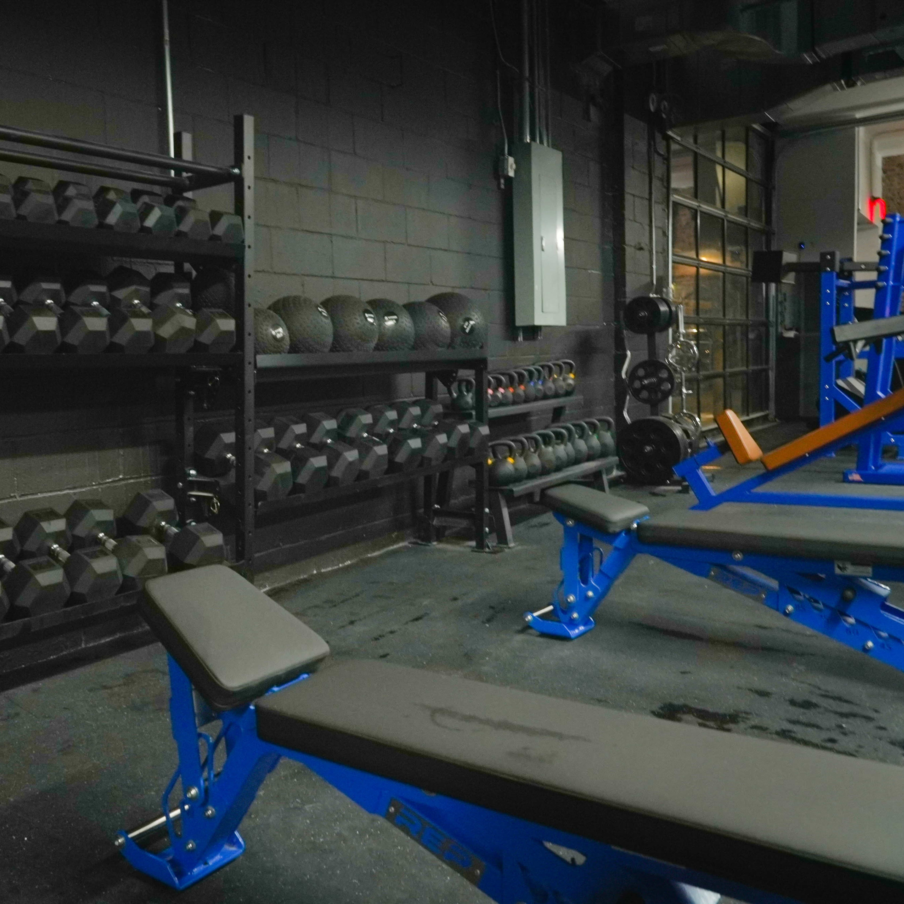 A fitness area with racks of dumbbells and several weight benches against a dark wall.