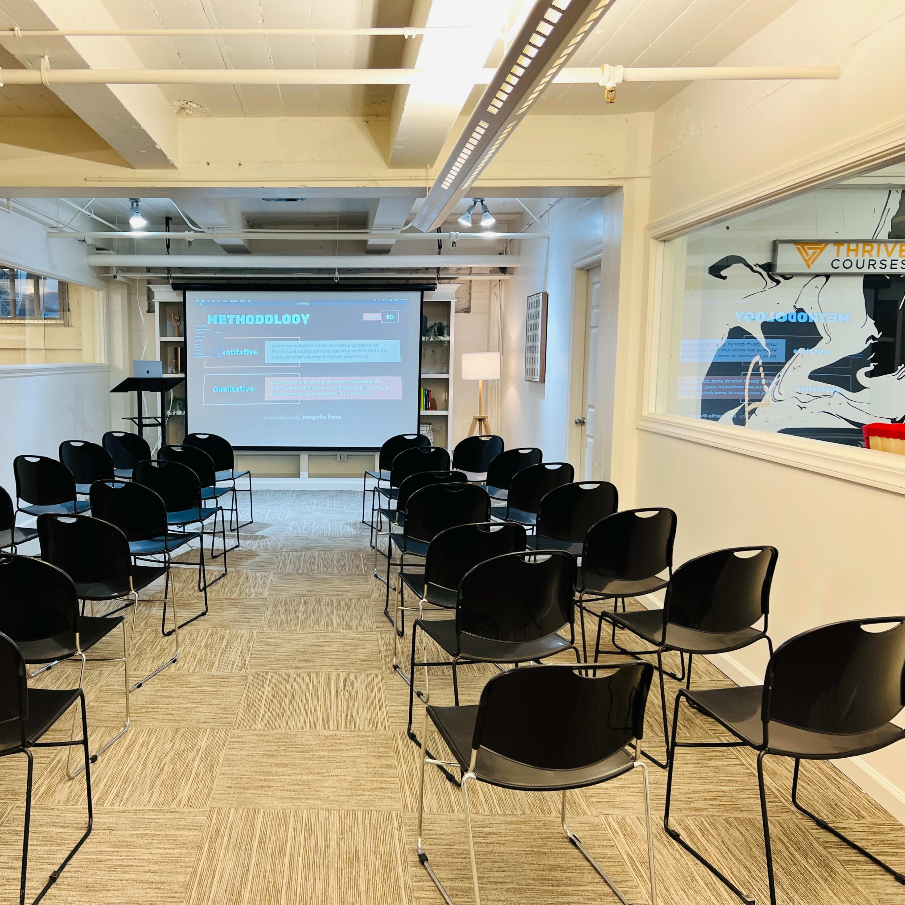 A row of black chairs is set up in a well-lit room facing a projection screen that displays the word "METHODOLOGY."