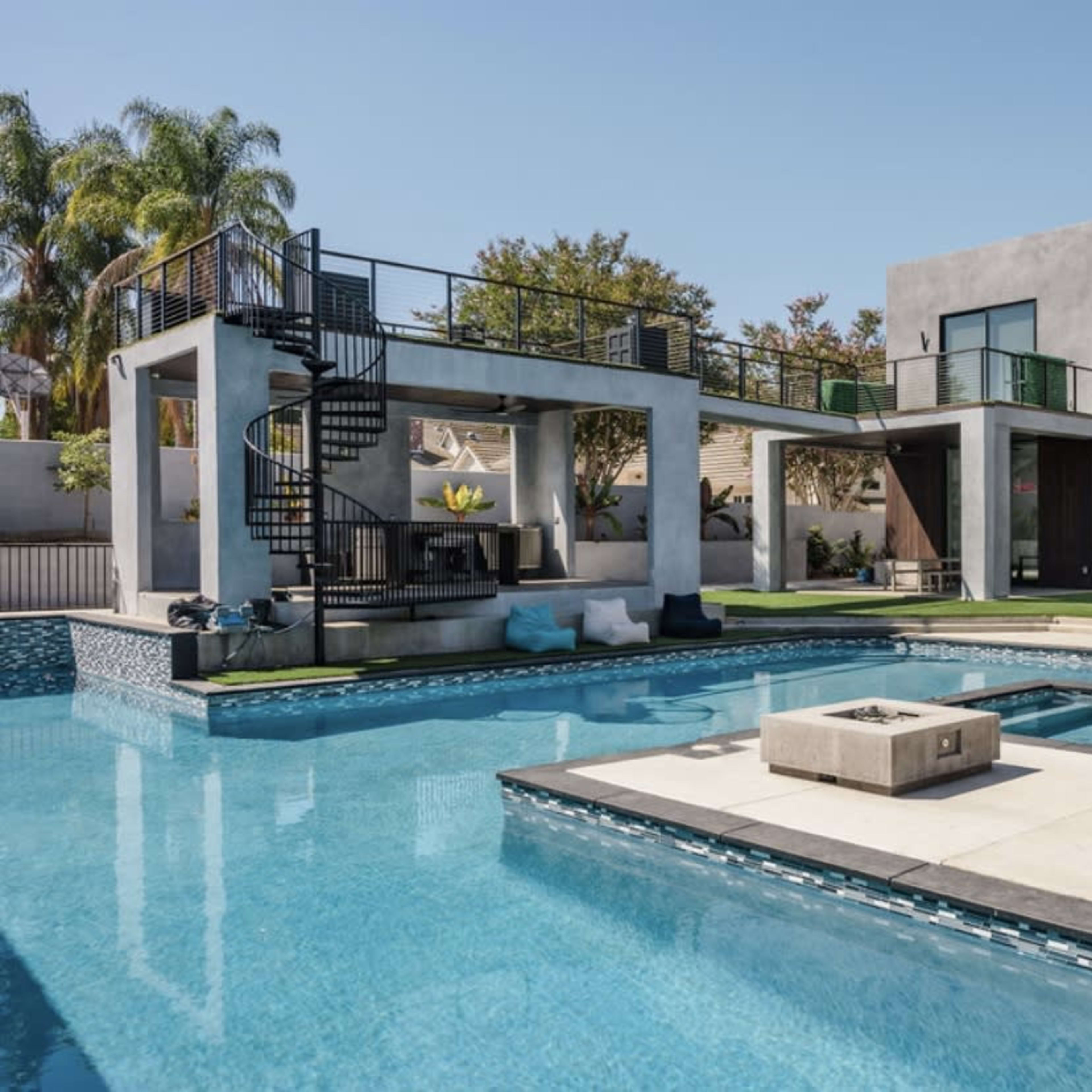 A modern home with two distinct buildings surrounding a swimming pool, featuring a spiral staircase and a landscaped yard.