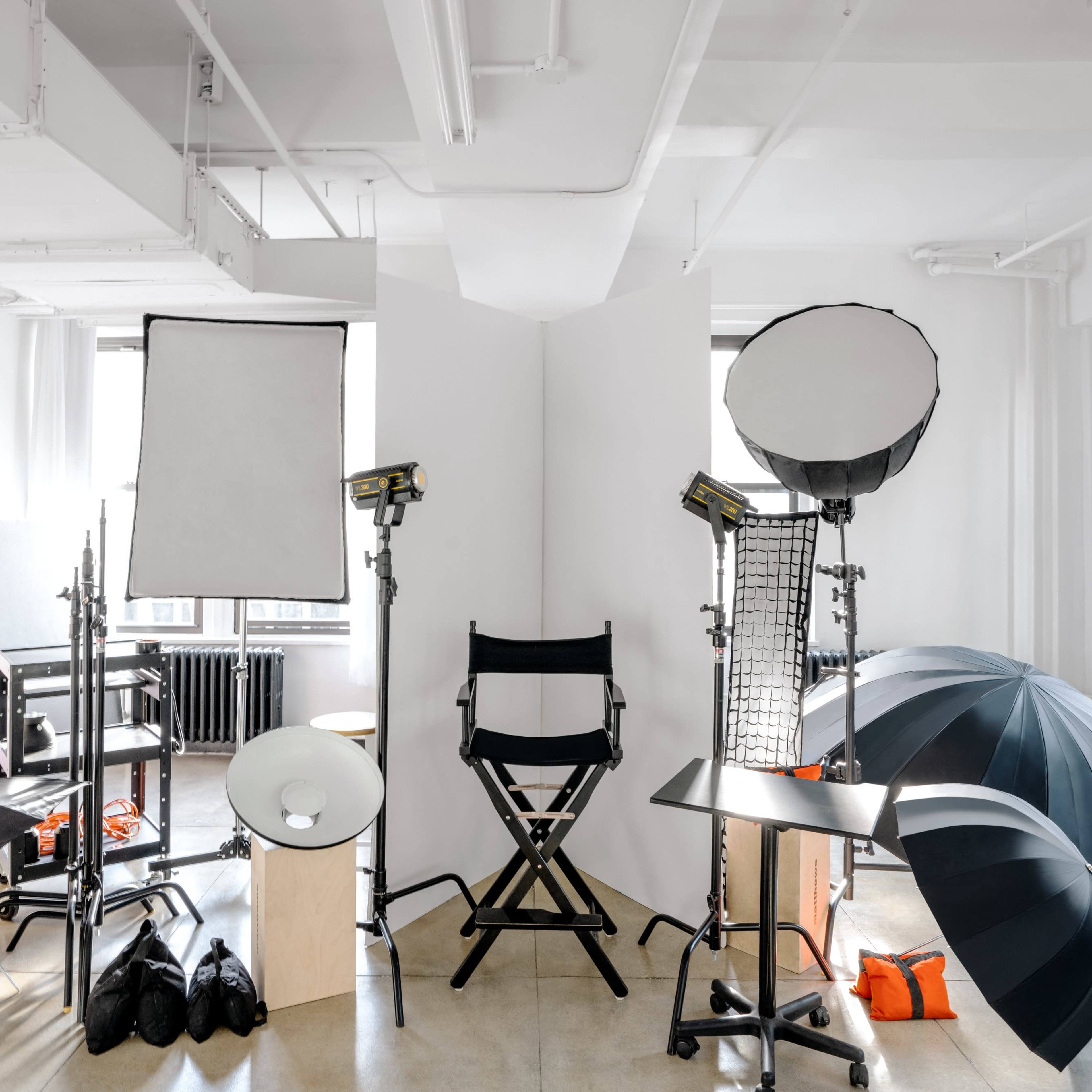 A photography studio setup features multiple light sources, reflectors, and a director's chair surrounded by various studio equipment.