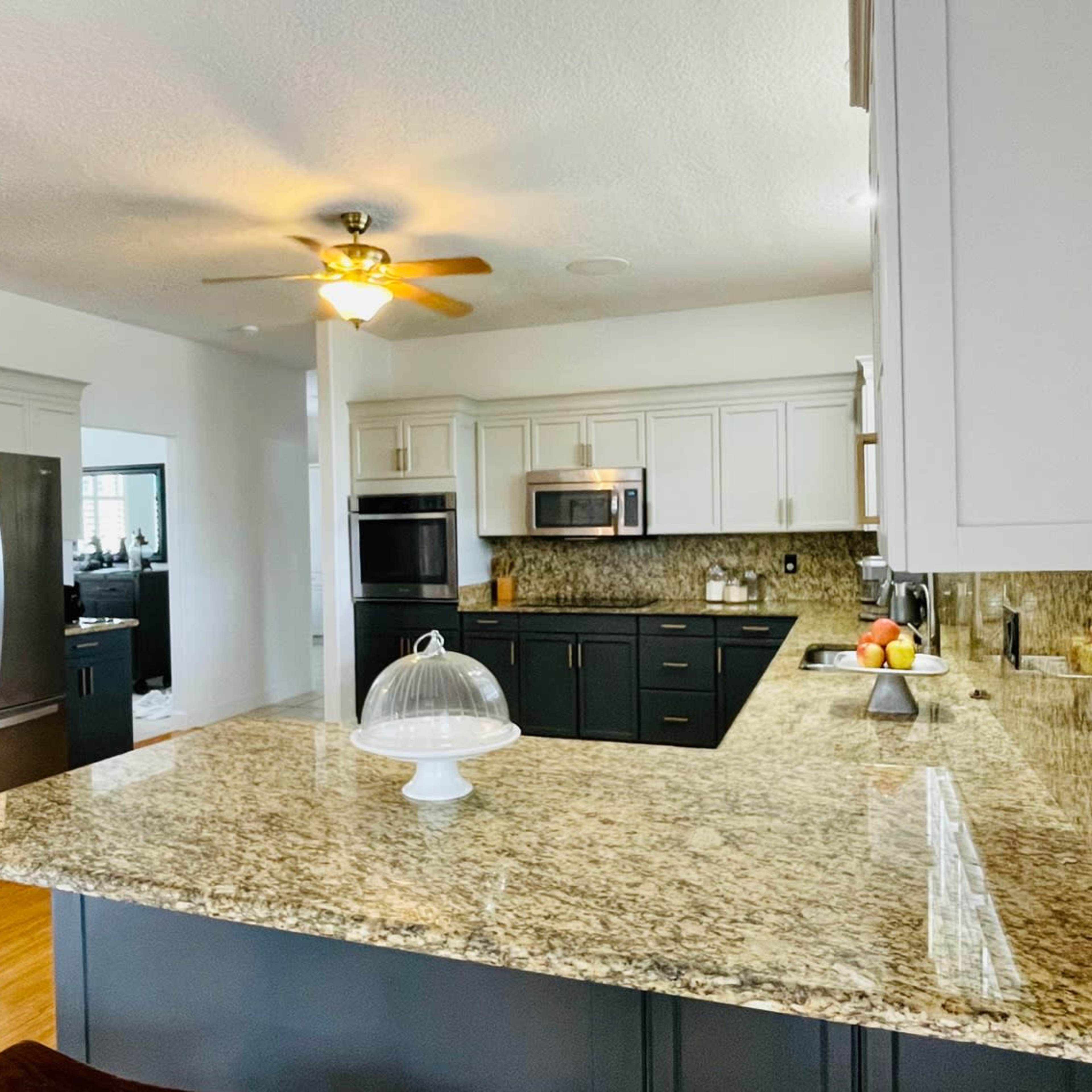 A modern kitchen with a granite countertop, stainless steel appliances, and a ceiling fan.