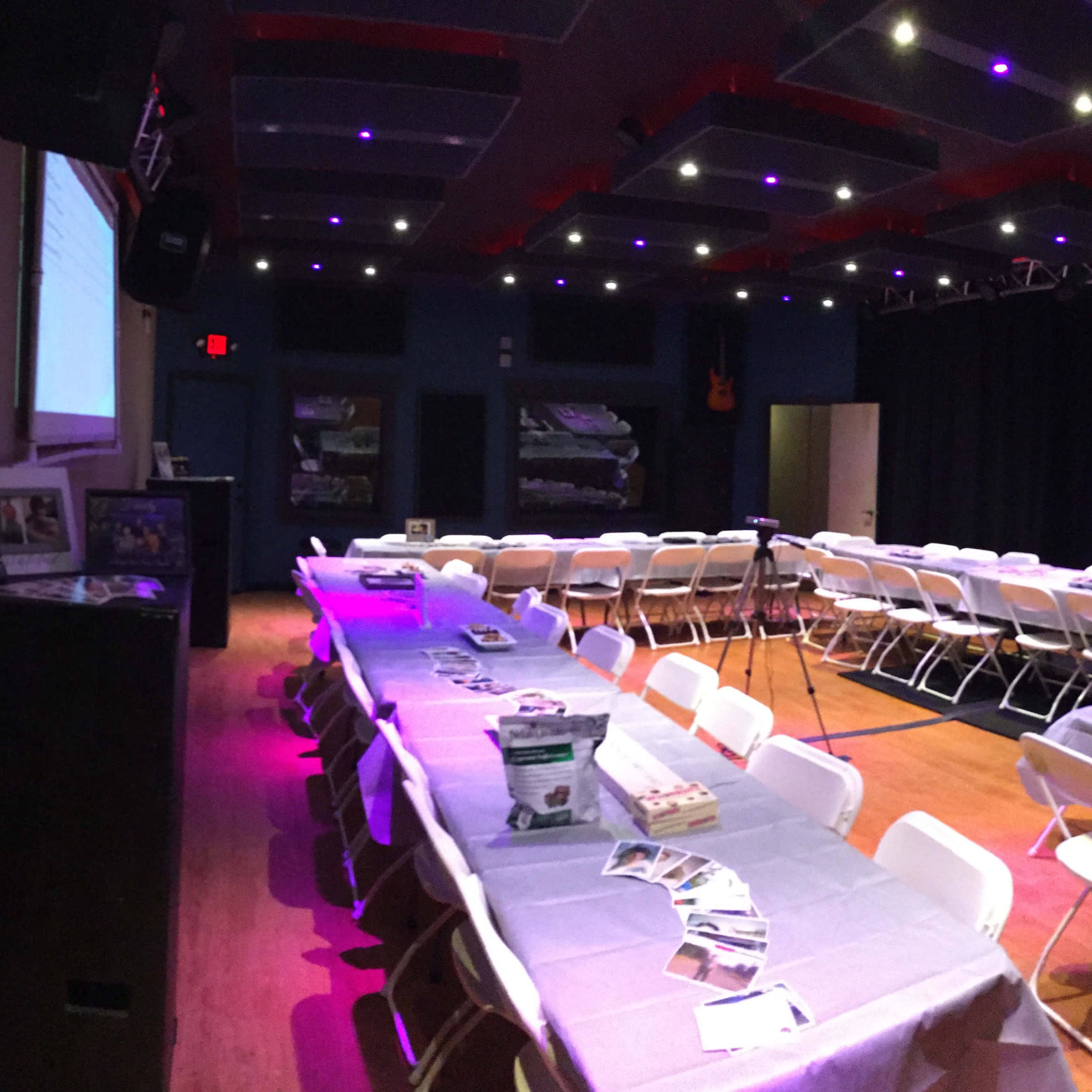 A spacious room is set up with white folding chairs arranged around a central area, decorated with gray tablecloths and promotional materials on each table.