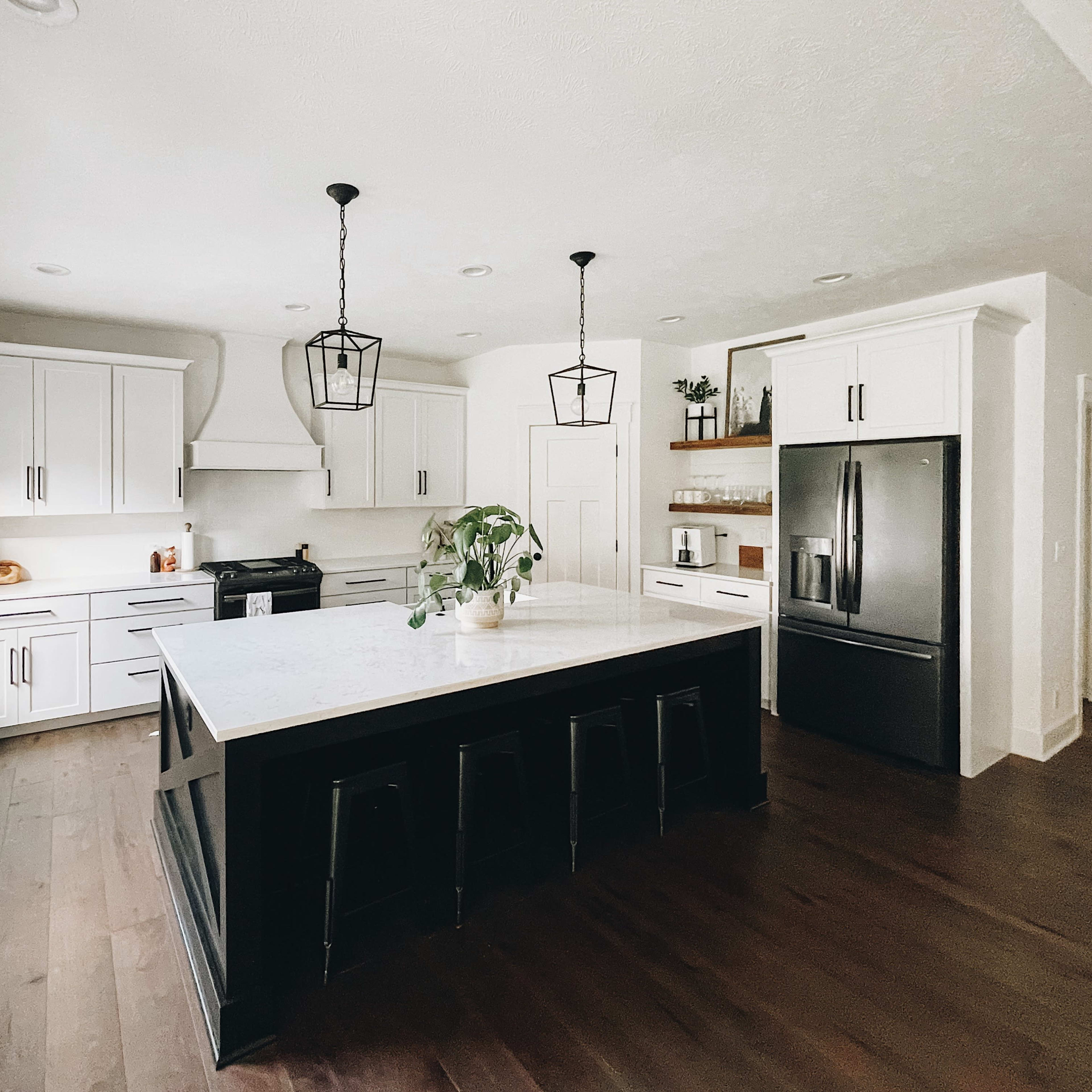 A modern kitchen featuring white cabinetry, a large island with a marble countertop, and black bar stools.