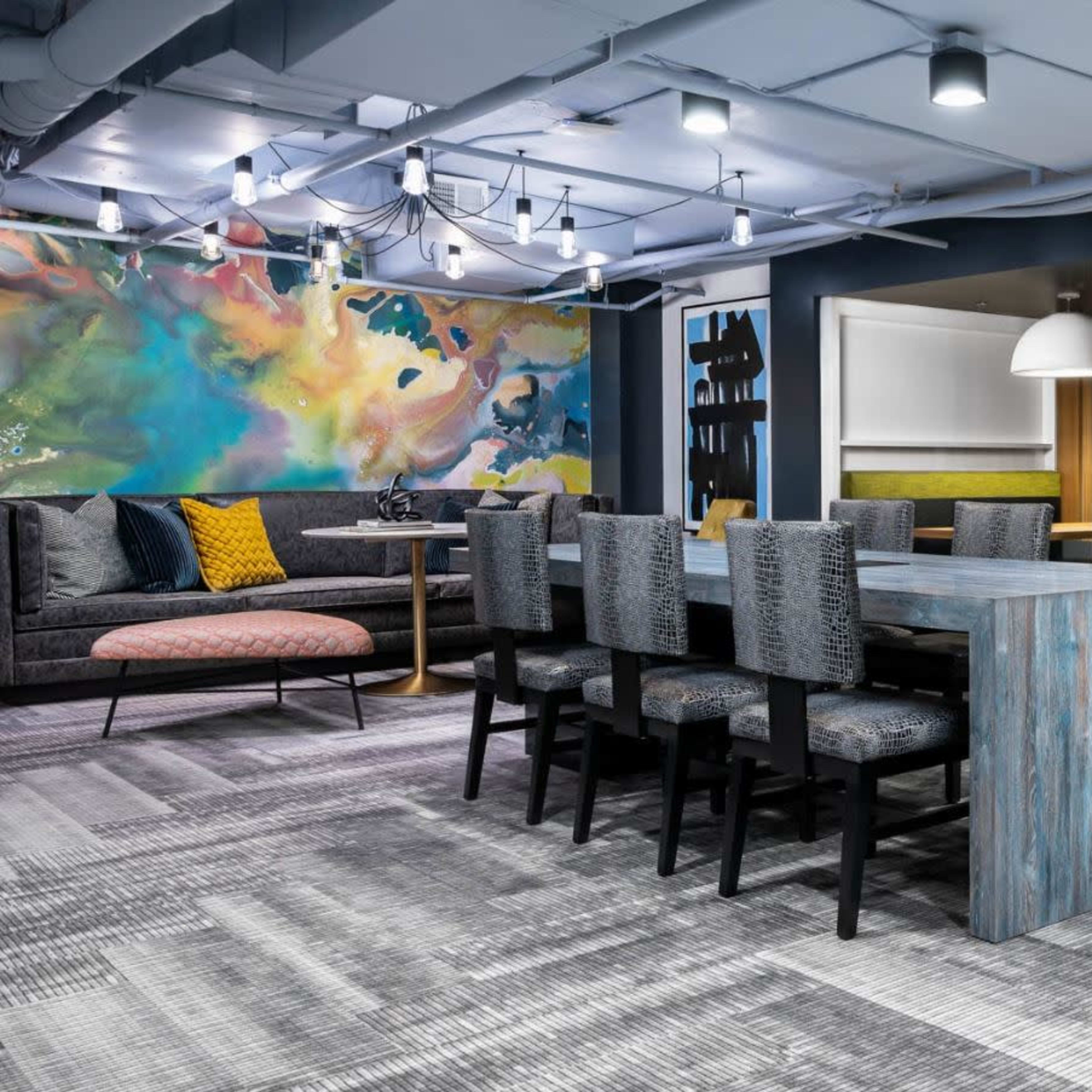 A modern coworking space featuring a long table with black chairs, colorful wall art, and private booth seating areas.