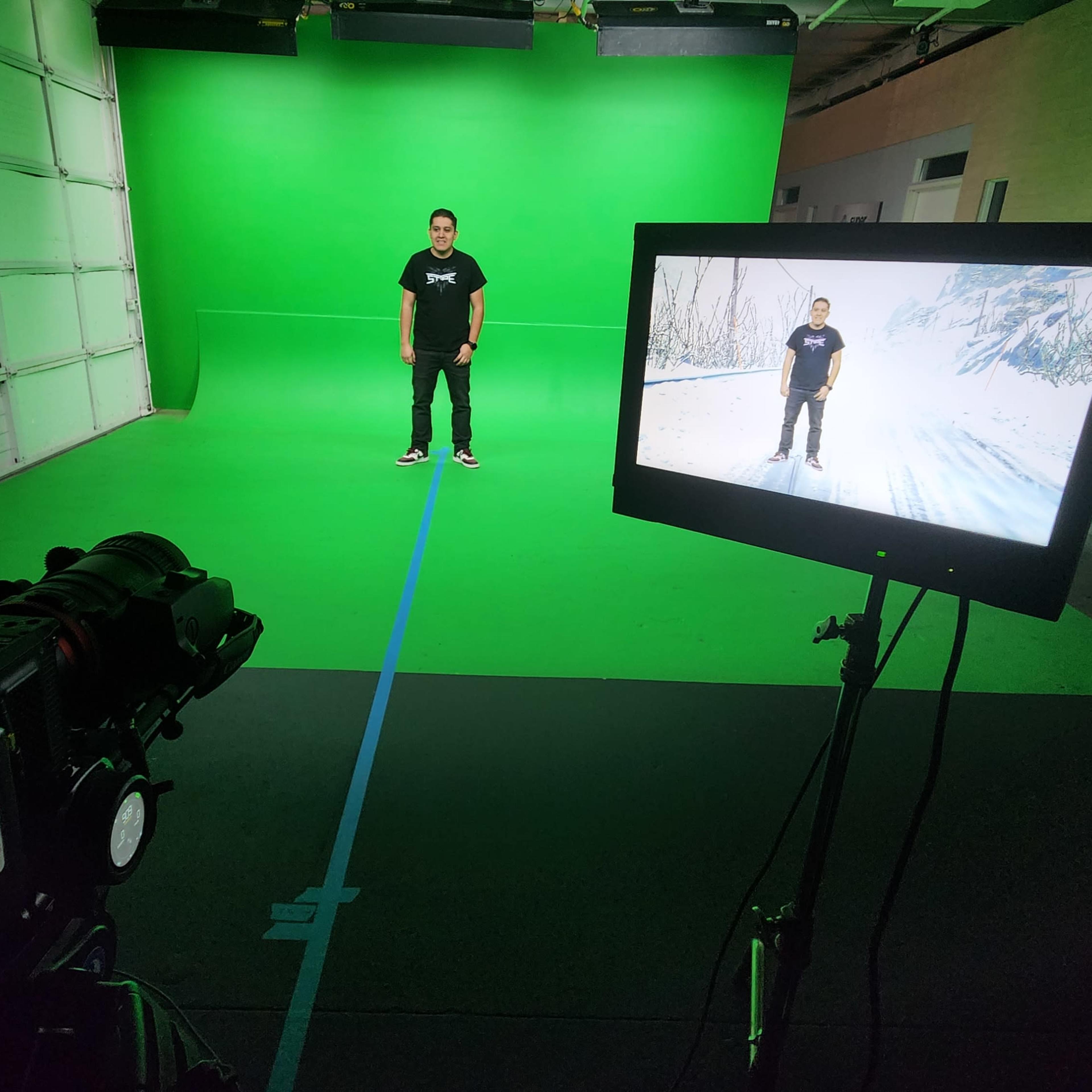 A person stands on a green screen stage while a camera and monitor display a winter scene.
