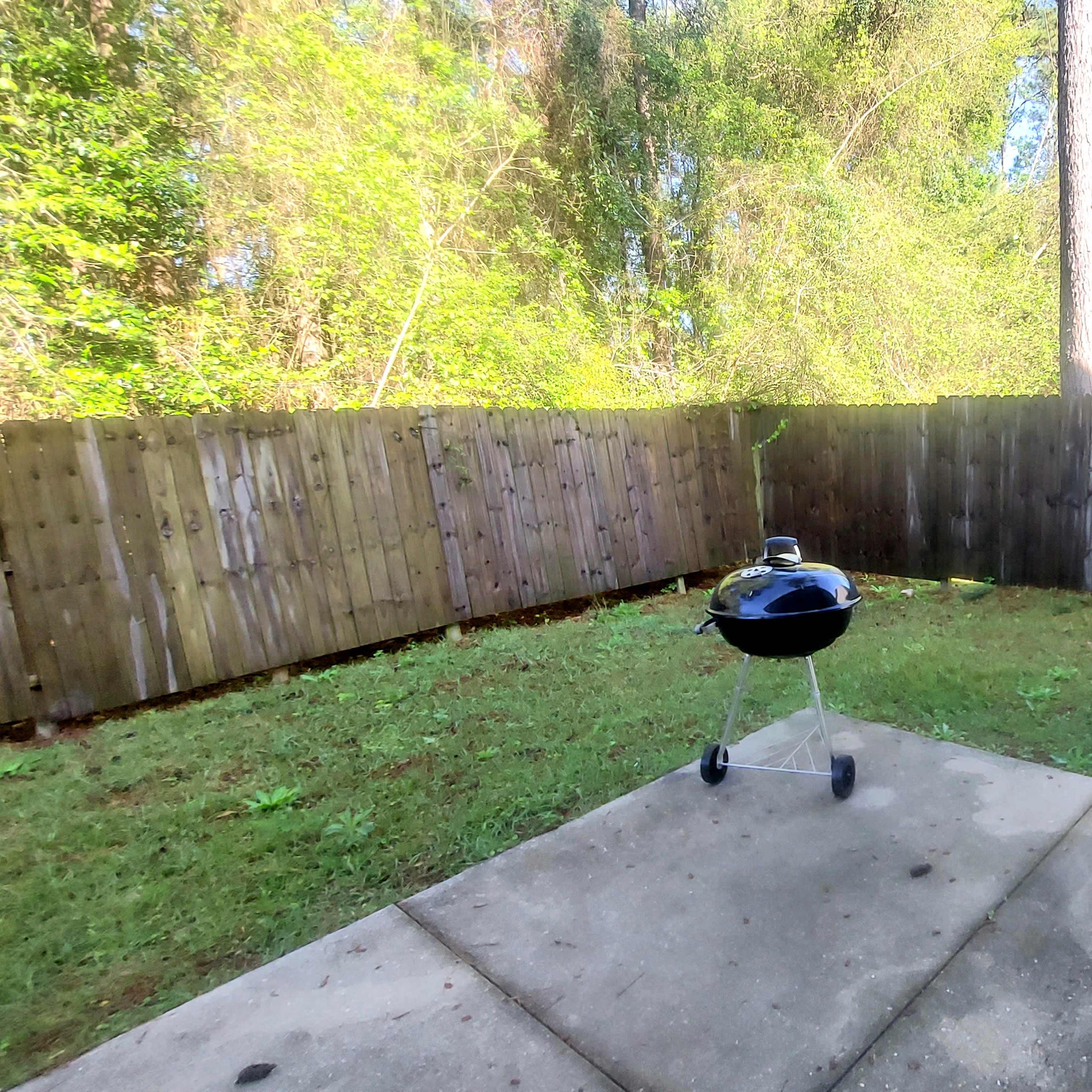 A small backyard with a grilling area on a concrete slab, bordered by a wooden fence and surrounded by trees.