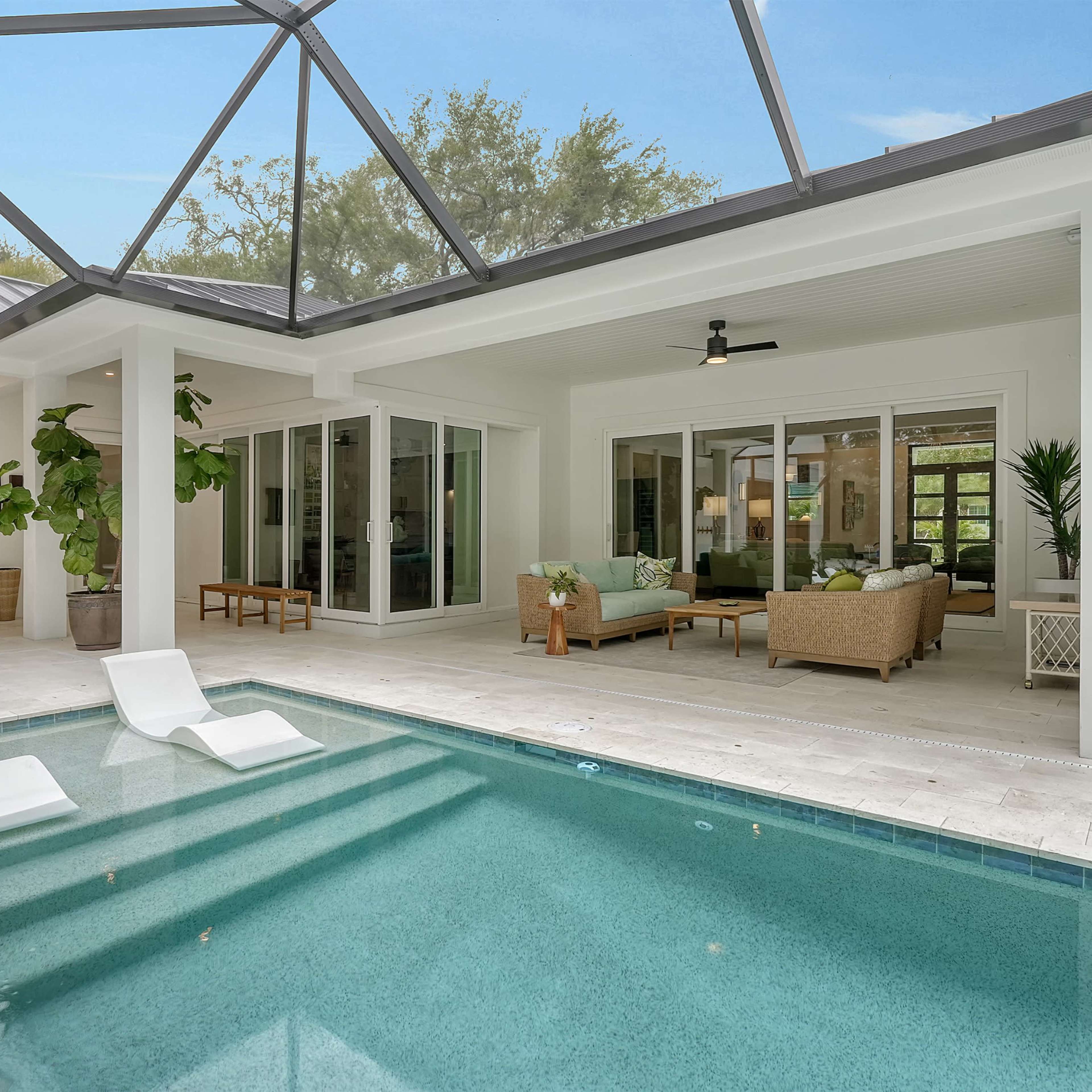 A modern home with a glass-enclosed patio and a swimming pool featuring two white lounge chairs.