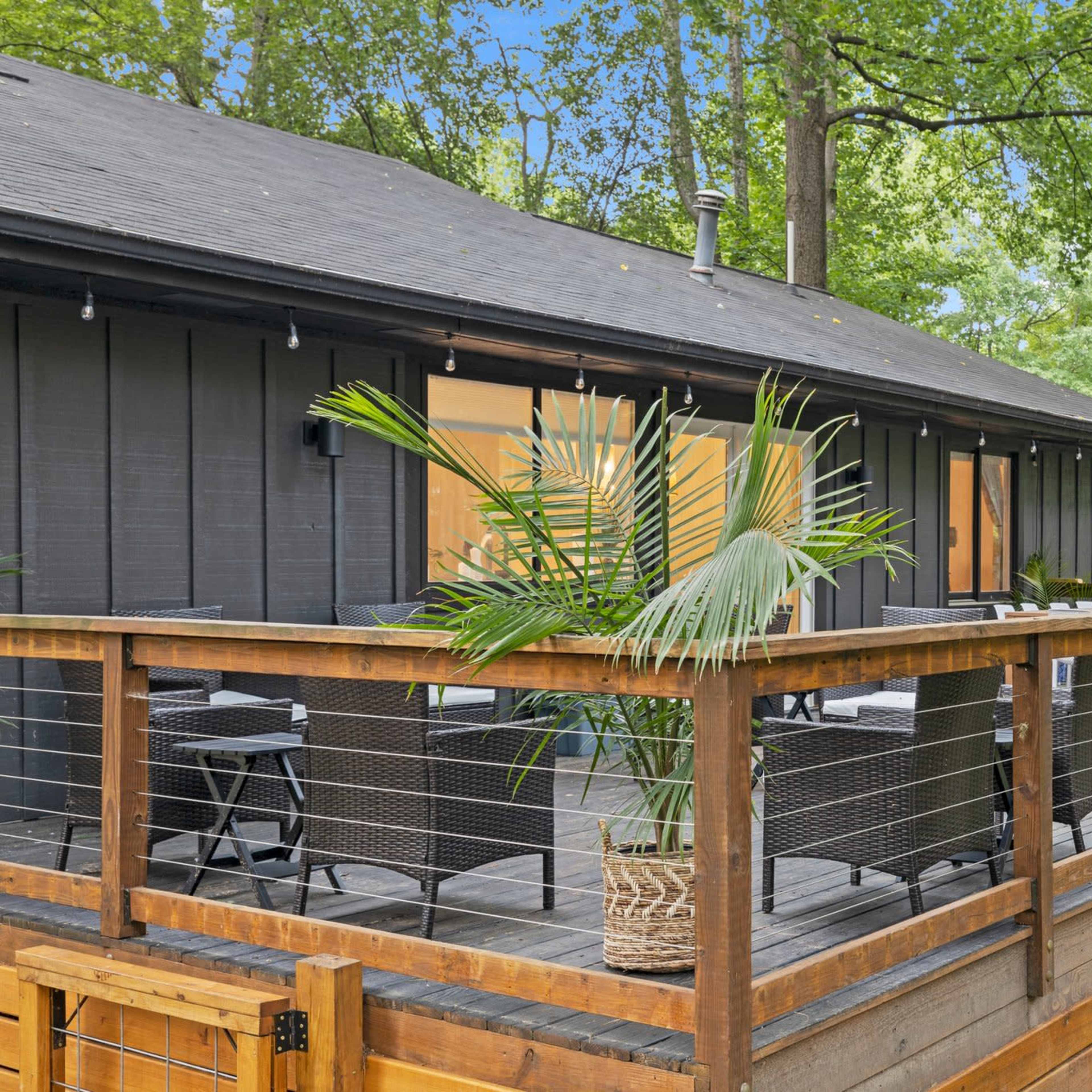A wooden deck with seating overlooks a yard surrounded by trees.