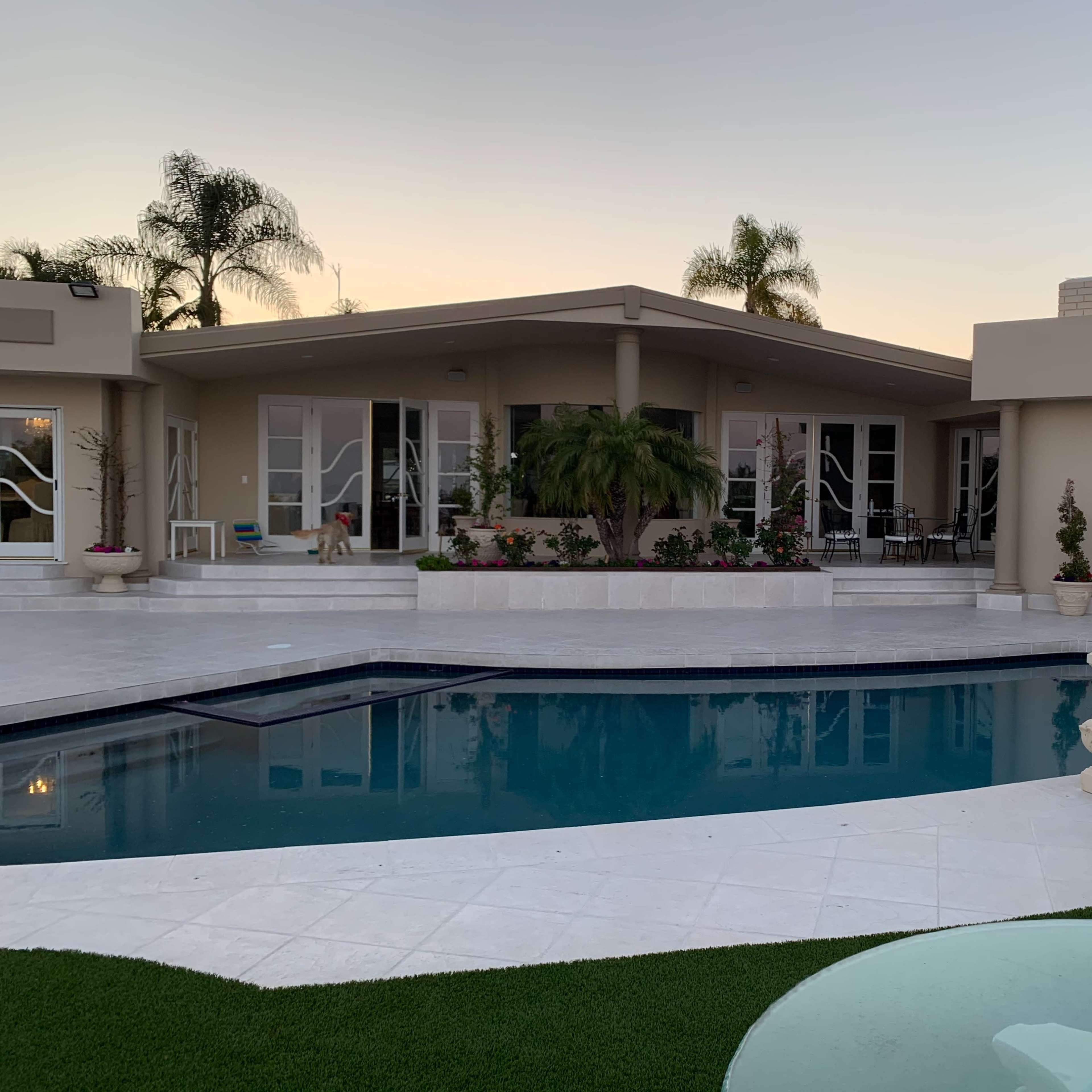 A modern house with a pool surrounded by palm trees and landscaped gardens.