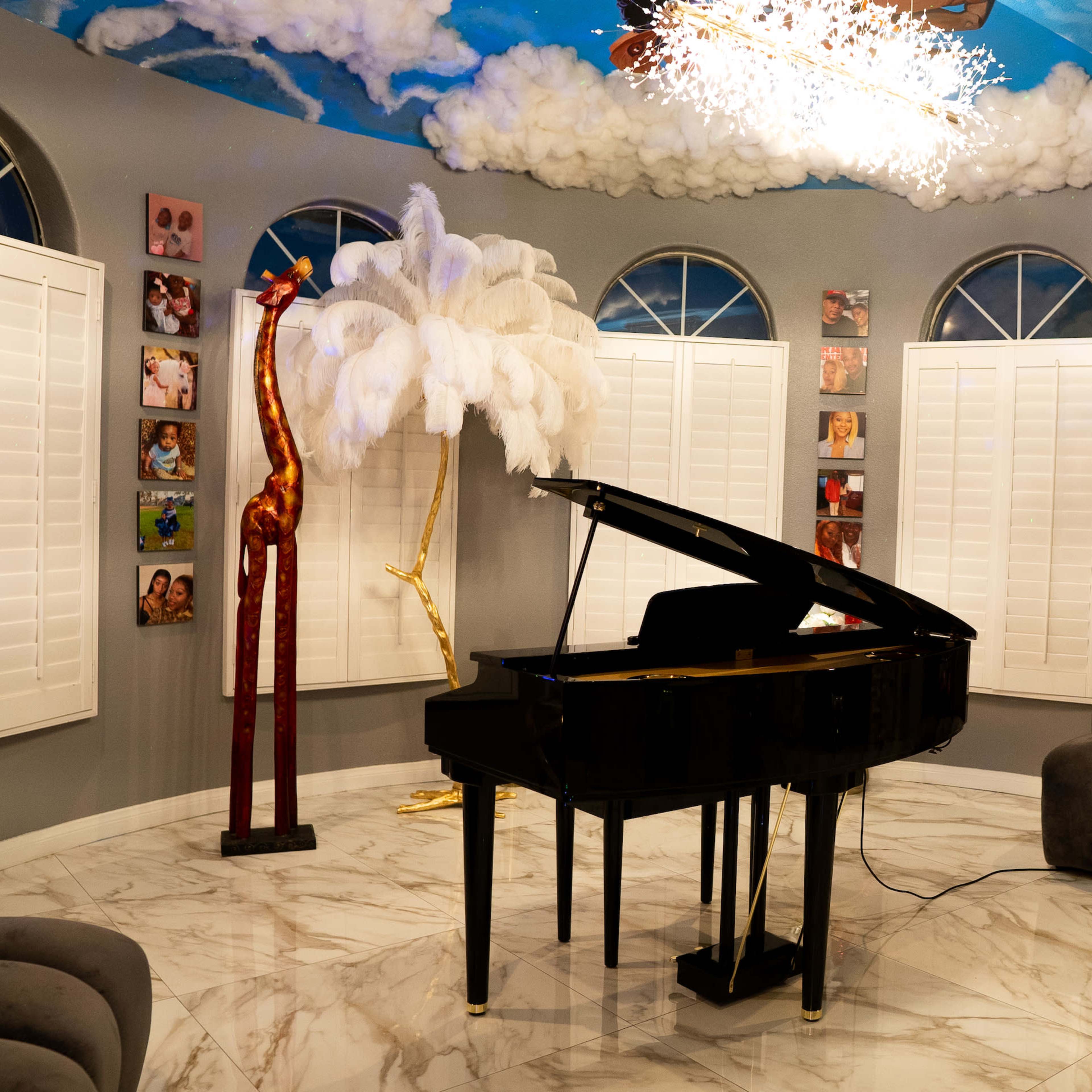 A grand black piano stands in a stylish room with cloud-painted ceilings, surrounded by light-colored furniture and decorative wall art.