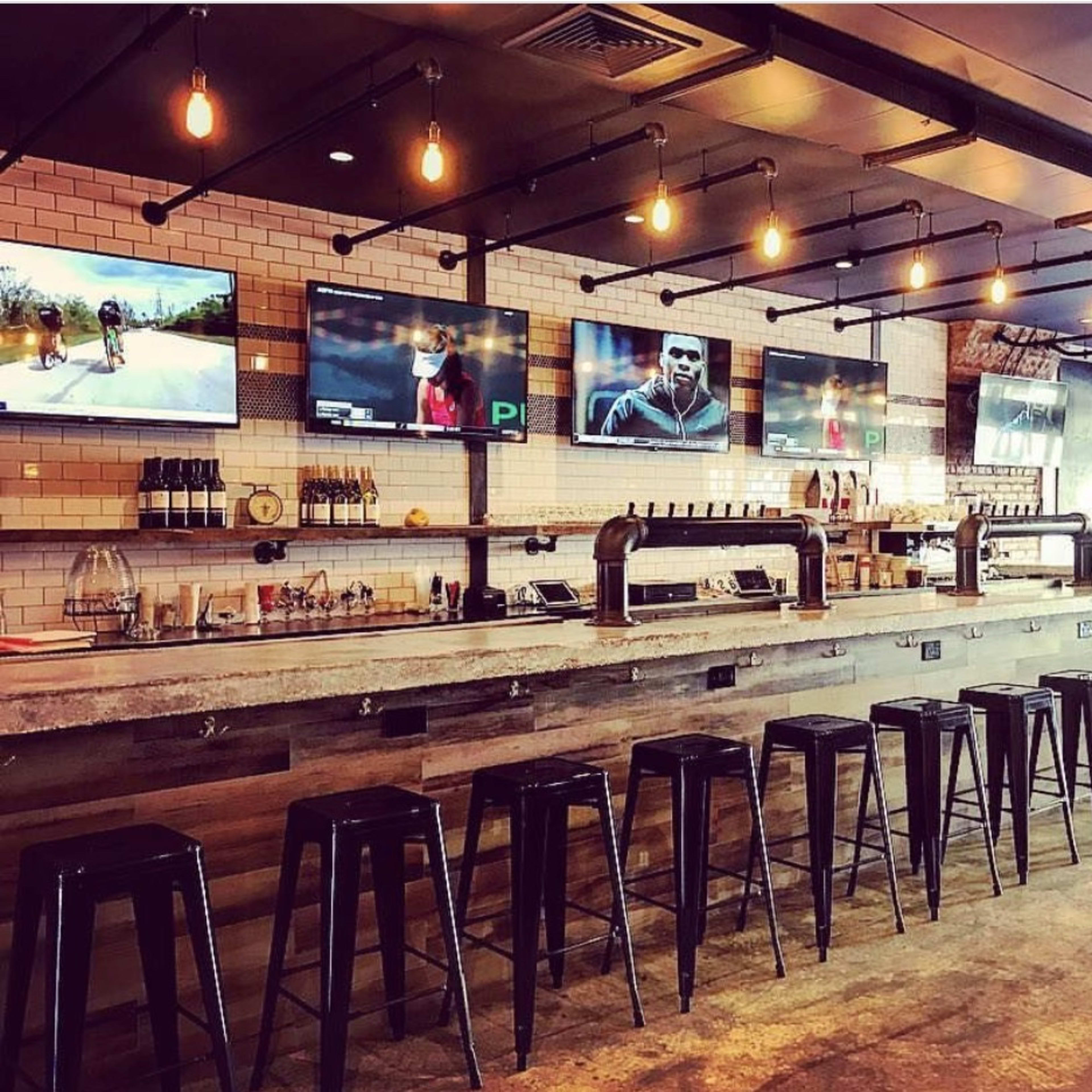 A bar with a concrete countertop, several bar stools, and multiple television screens displaying various sports events.