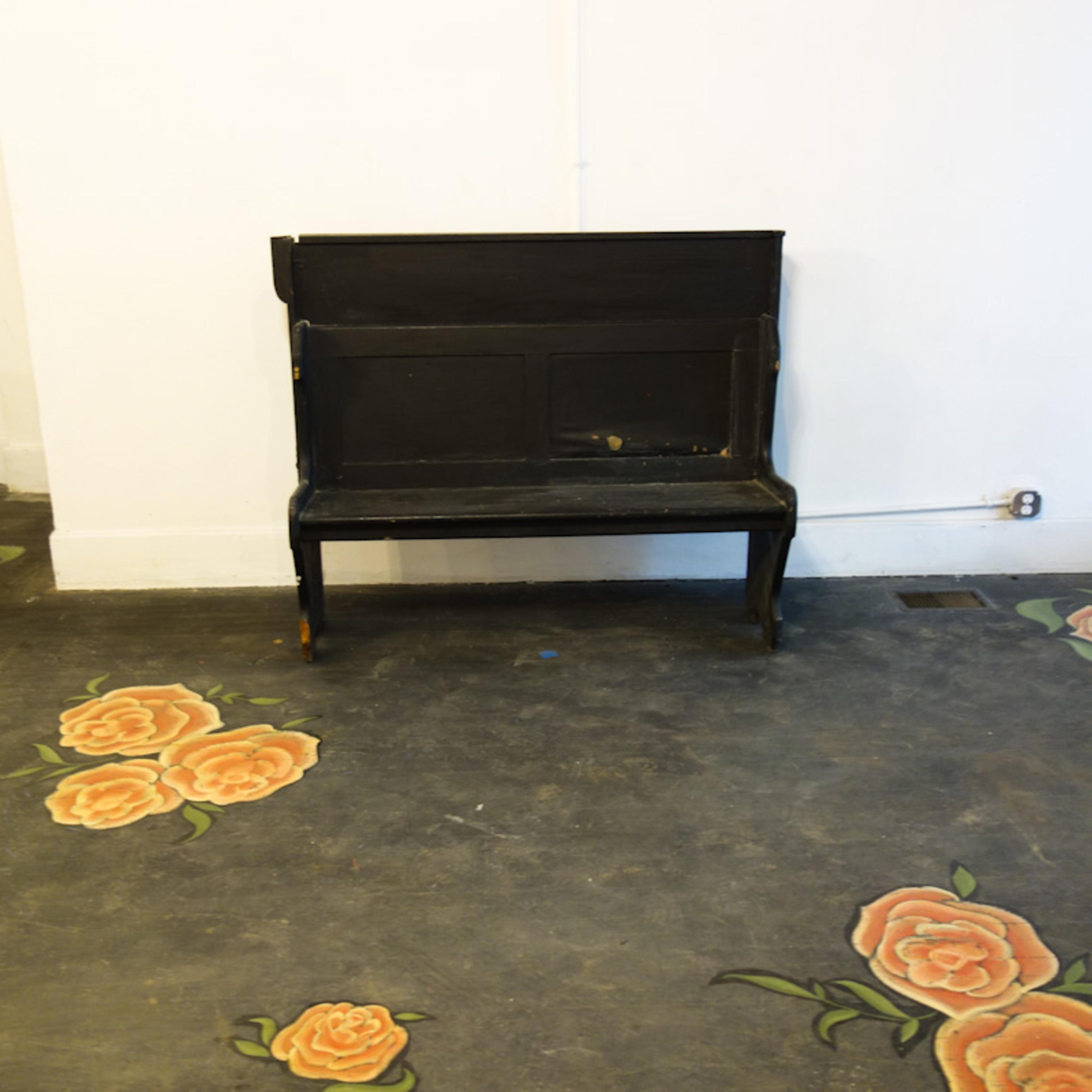 A black wooden bench is positioned in the center of a room with floral designs painted on the floor around it.