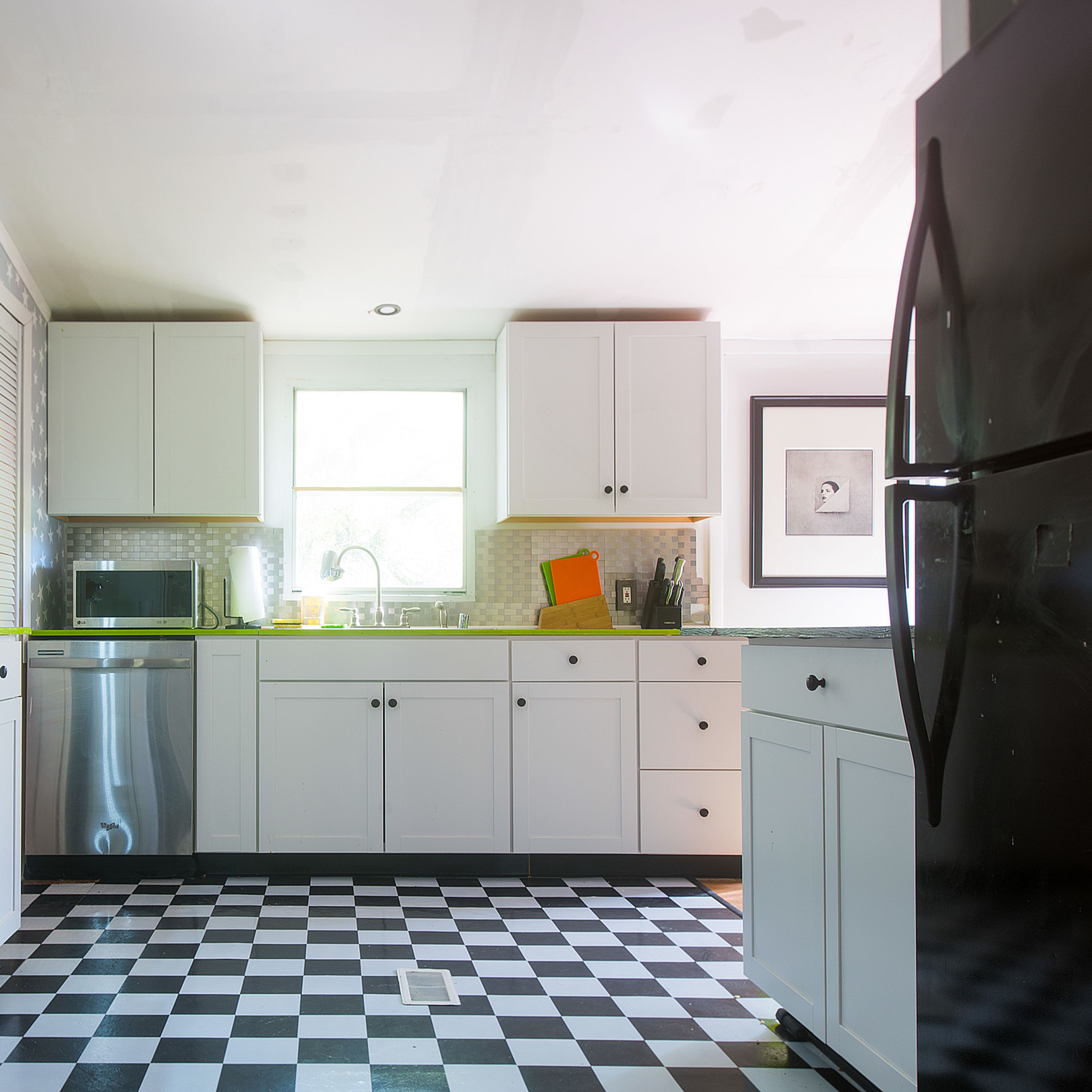 A modern kitchen with black and white checkered flooring, white cabinets, and stainless steel appliances.