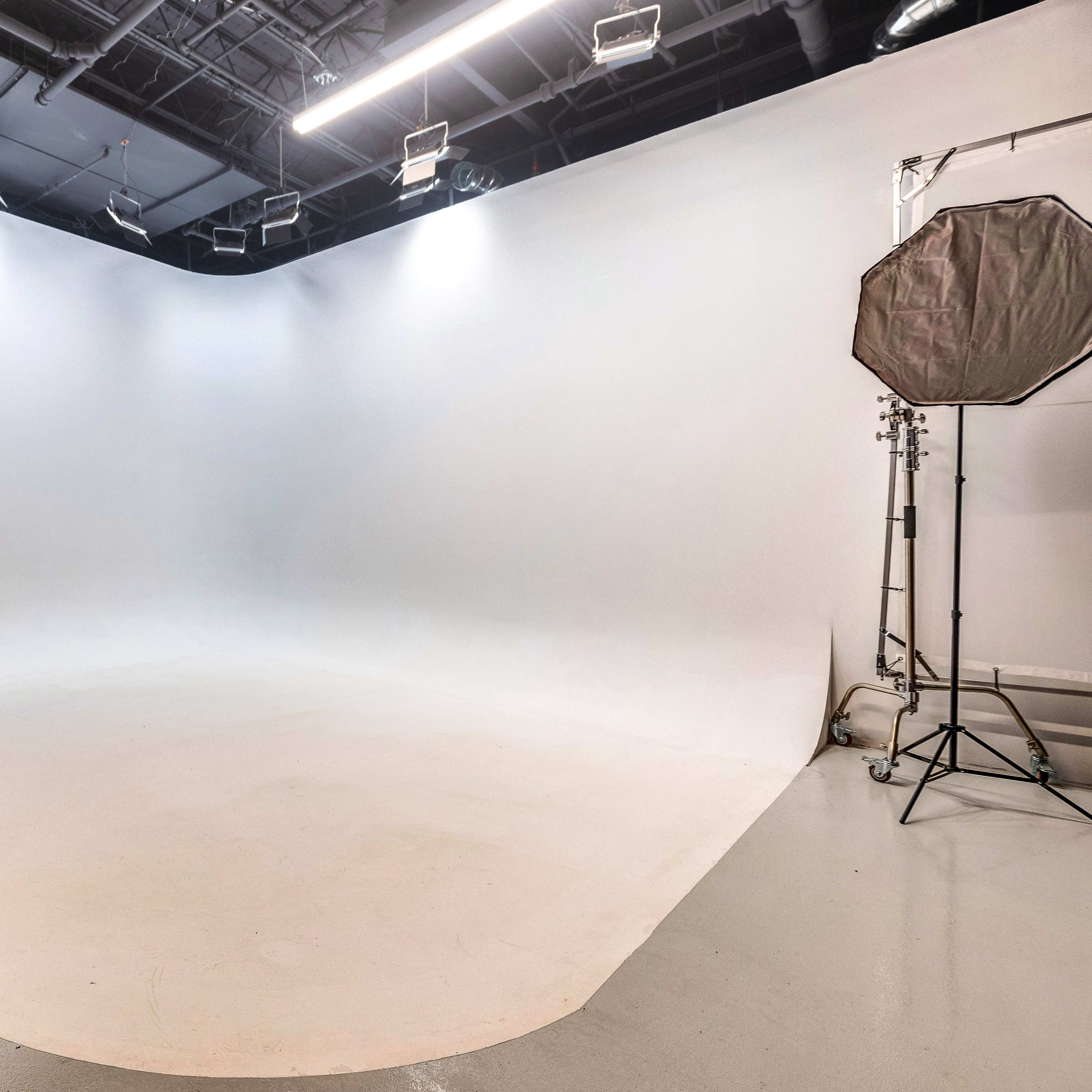 A large, empty photography studio with a seamless white backdrop and soft lighting equipment.