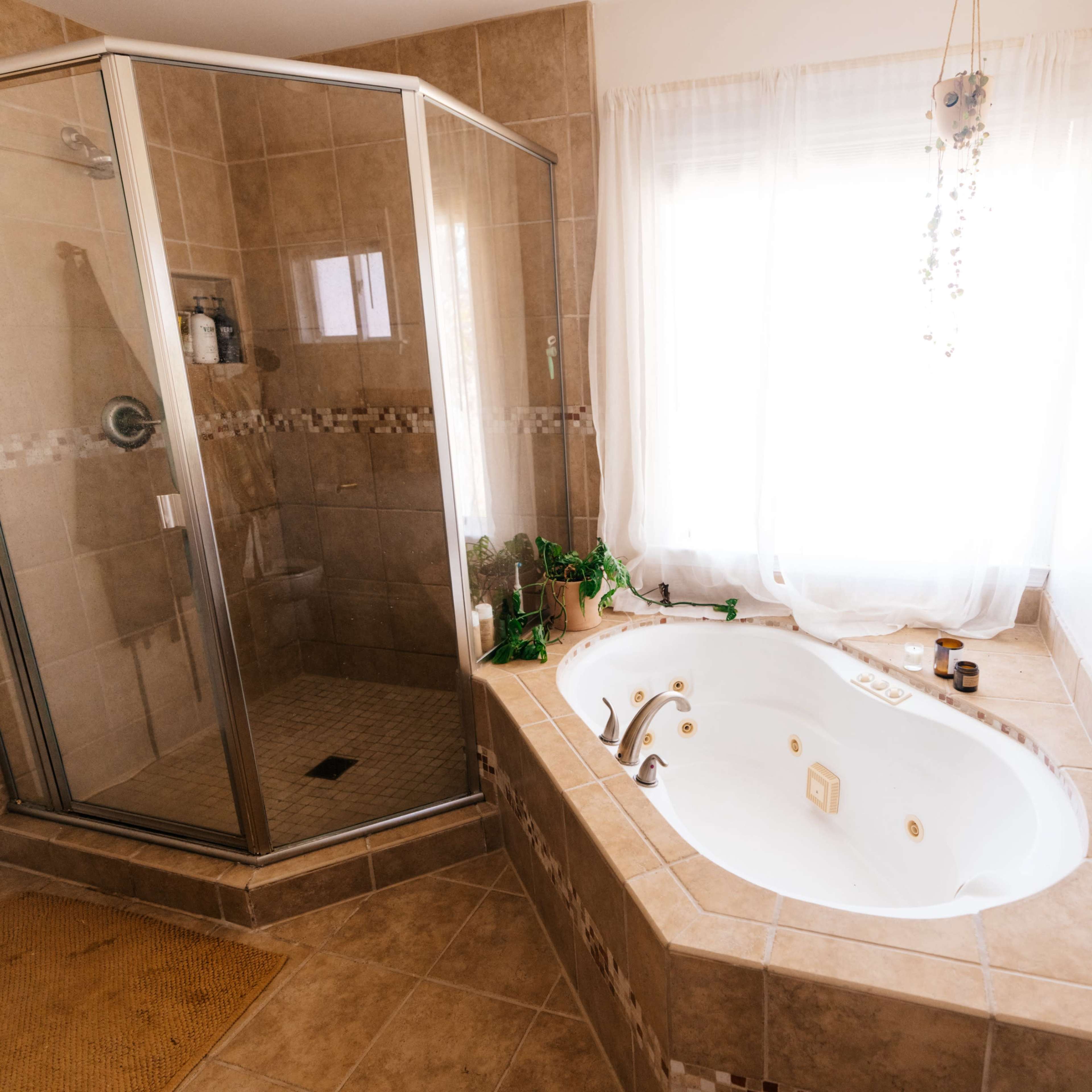 A bathroom featuring a glass shower enclosure, a corner jetted tub, and large tiled surfaces.