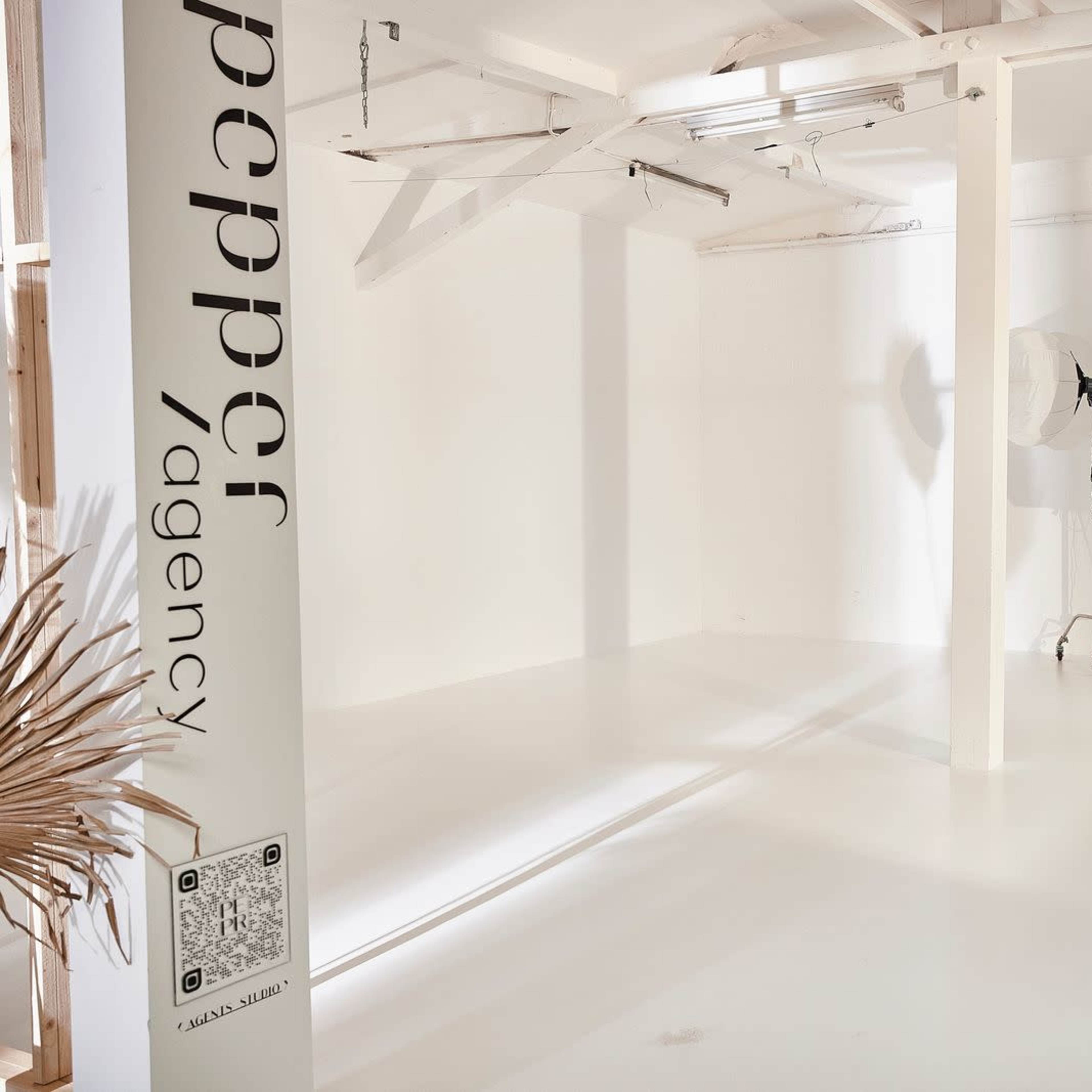A minimalistic studio space with white walls, a backdrop setup, a large softbox on a stand, and a low table.