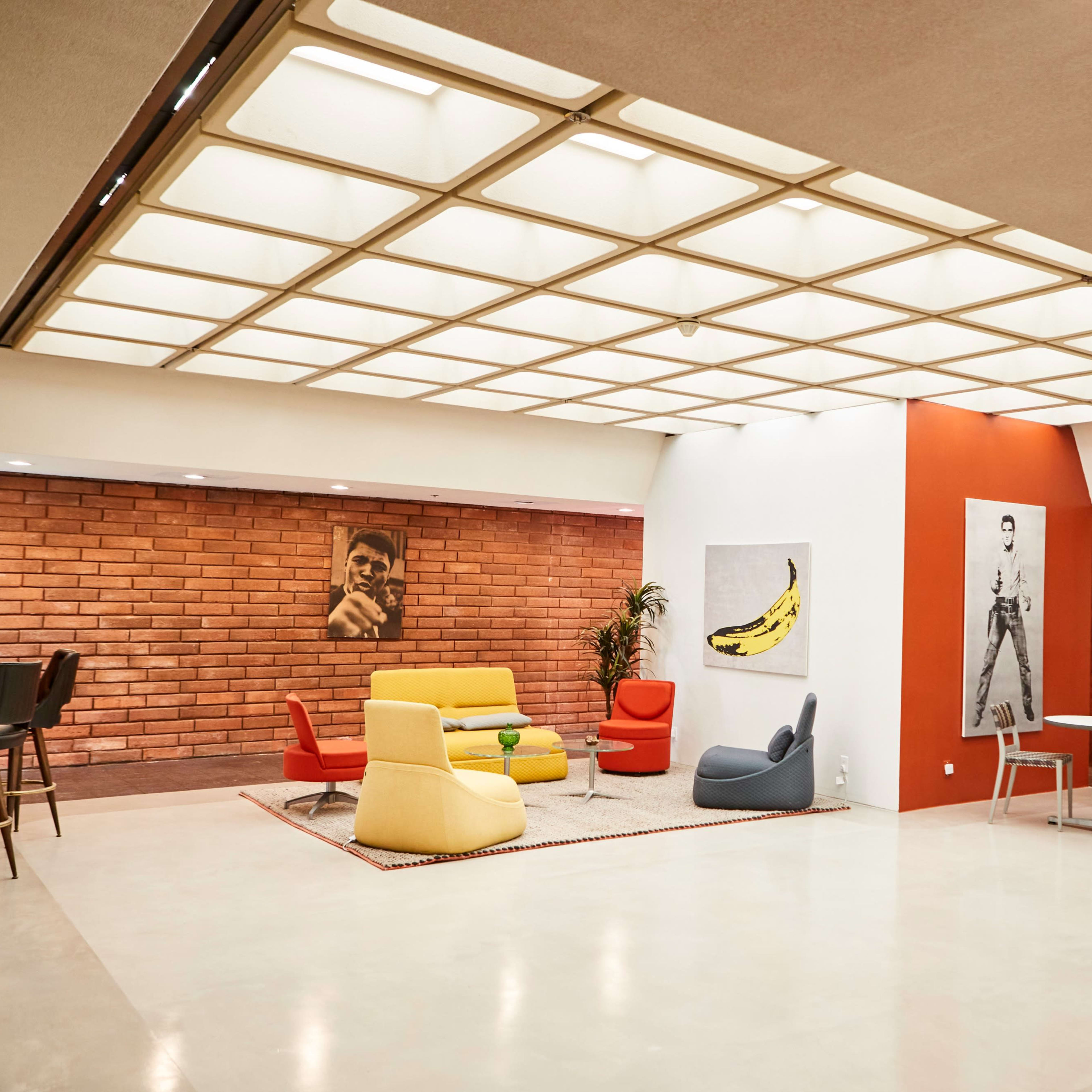 A modern lounge area with colorful seating, a brick wall, and a large ceiling feature providing ambient light.