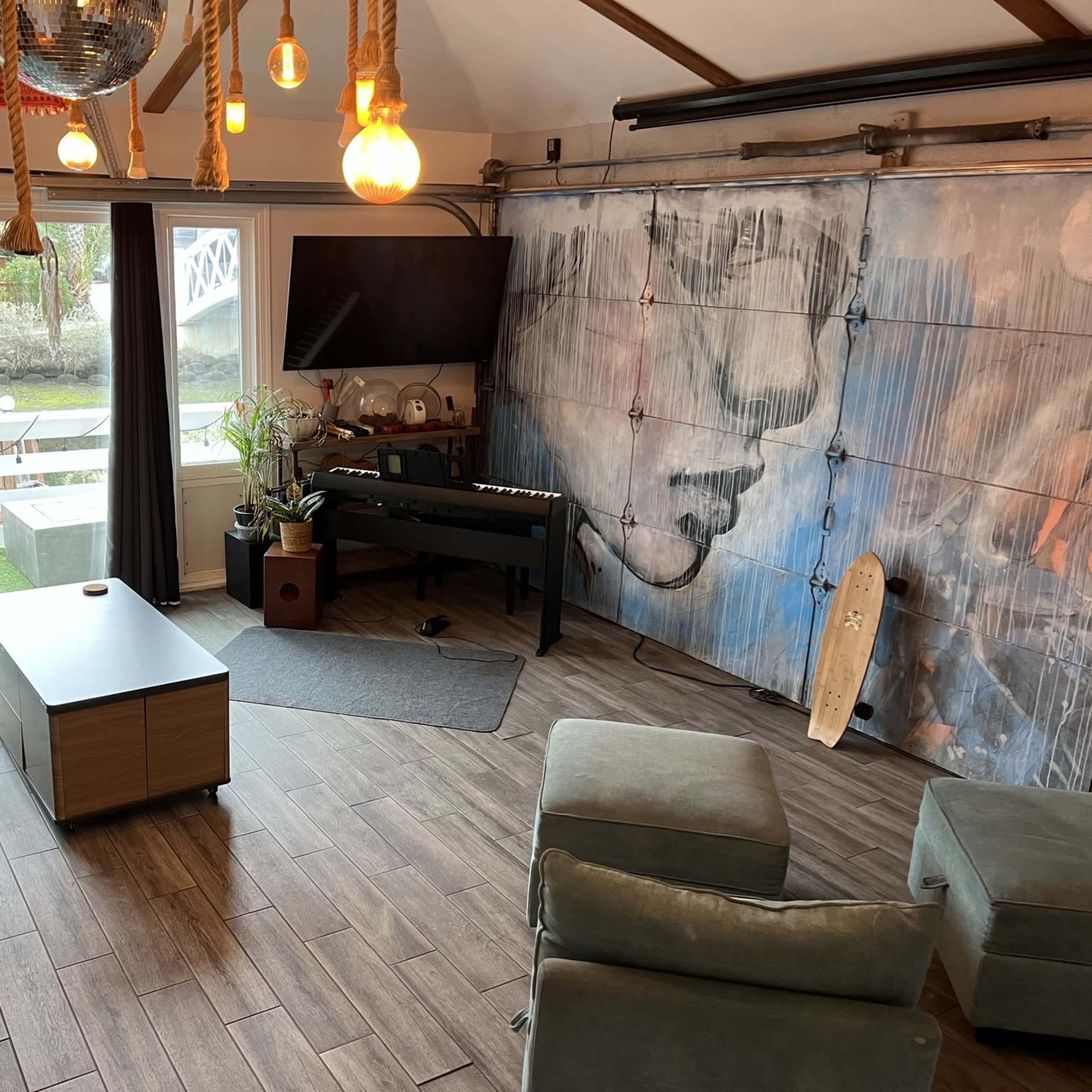 A modern living space with a large window, a television mounted on the wall, a piano, and a colorful mural.