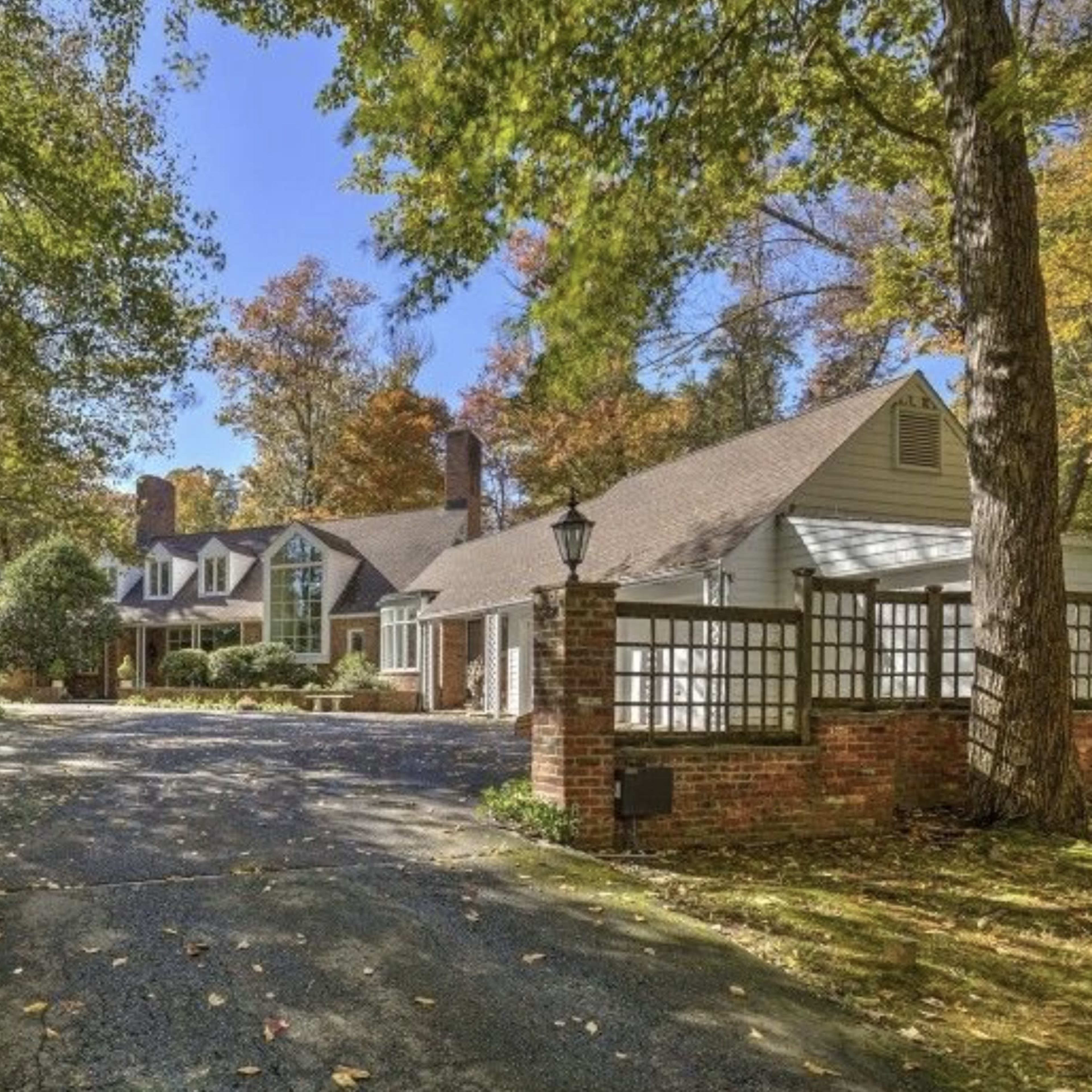A large, traditional-style home set back from a tree-lined driveway surrounded by autumn foliage.
