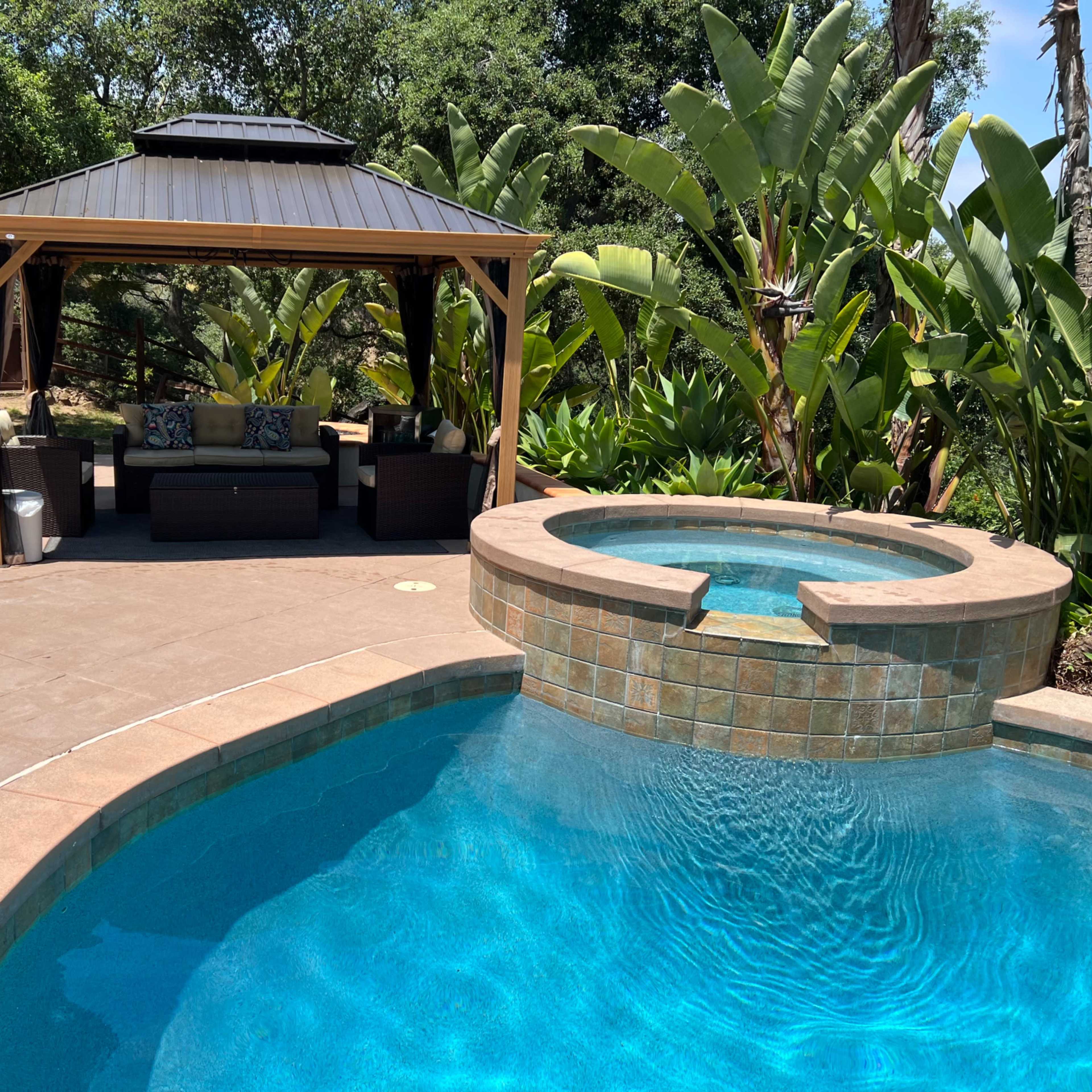 A landscaped outdoor area featuring a swimming pool, a spa, and a covered gazebo with seating.