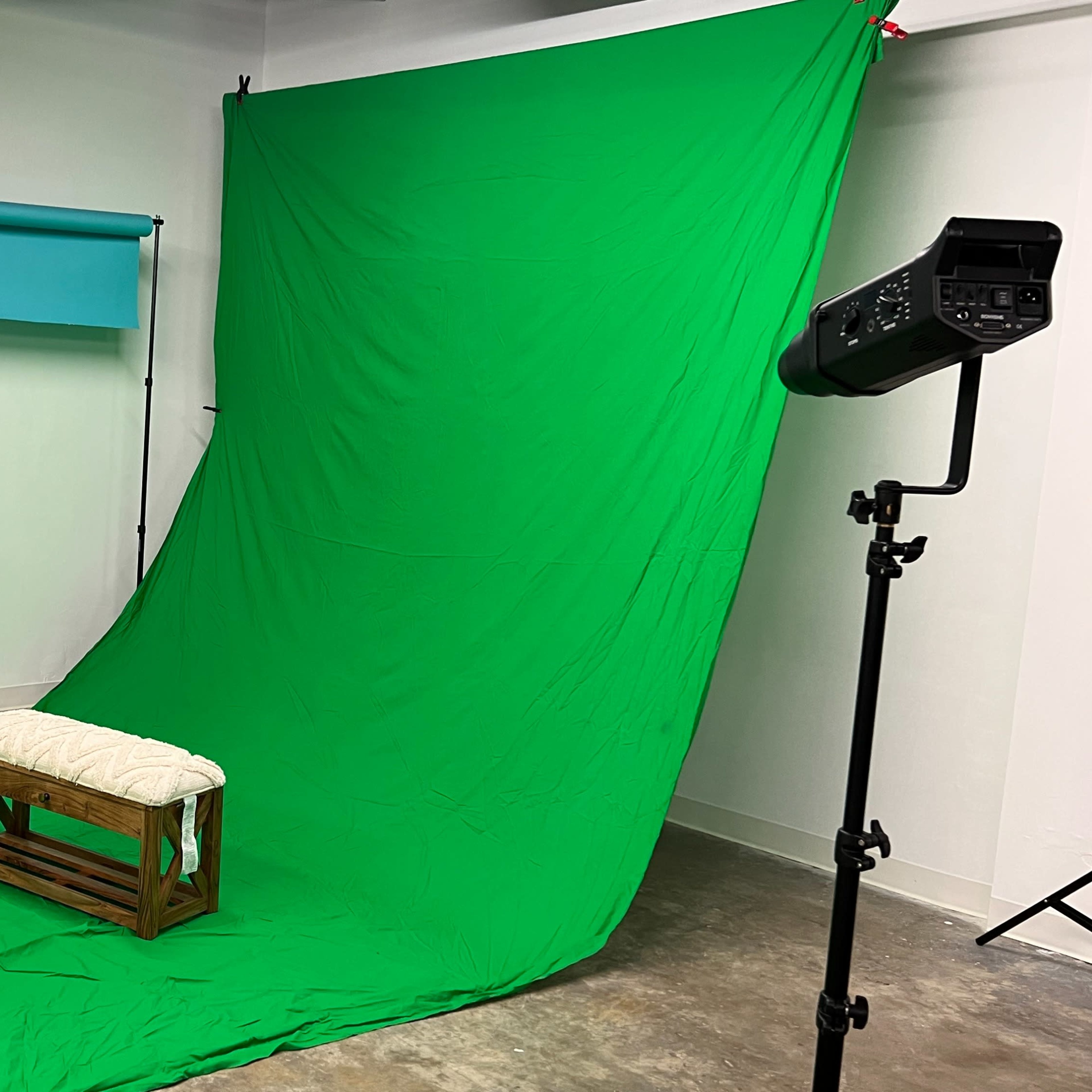 A photography studio with a green backdrop, a blue overhead screen, and lighting equipment positioned around a wooden bench.