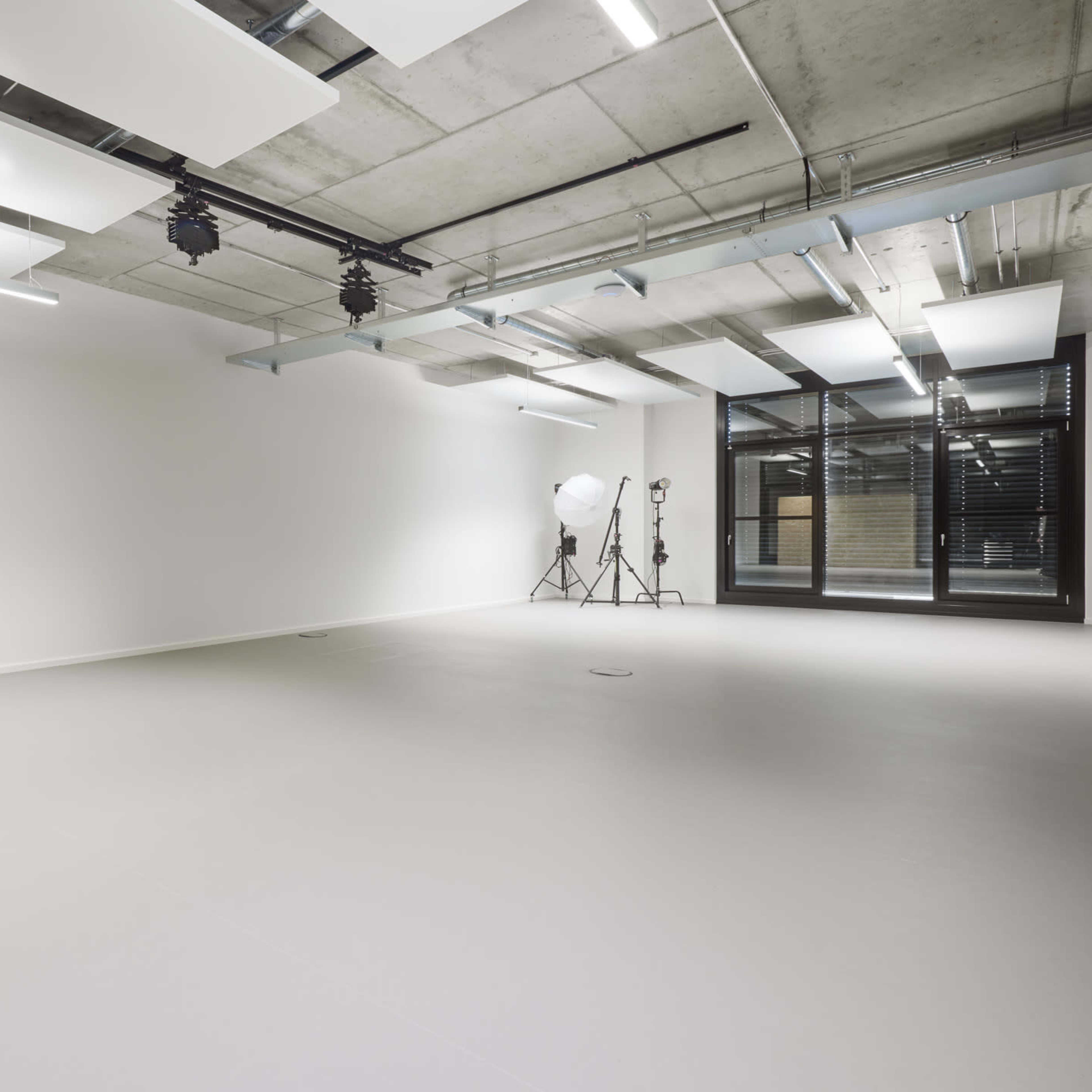 A spacious, empty room with concrete walls, industrial lighting, and photography equipment in the corner.
