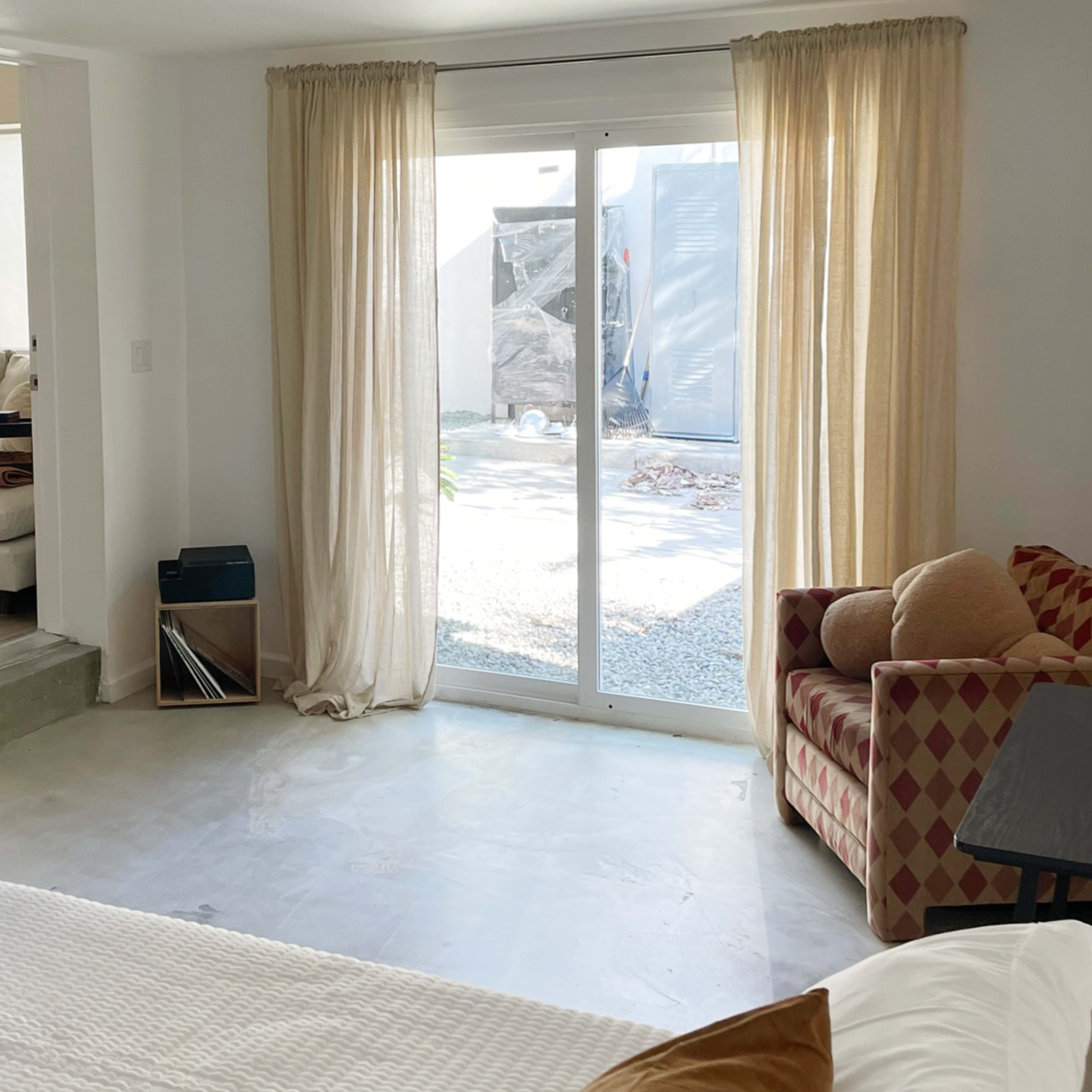 A sunlit bedroom features a bed, a mirror on the wall, a couch, and sliding glass doors leading to a patio area.